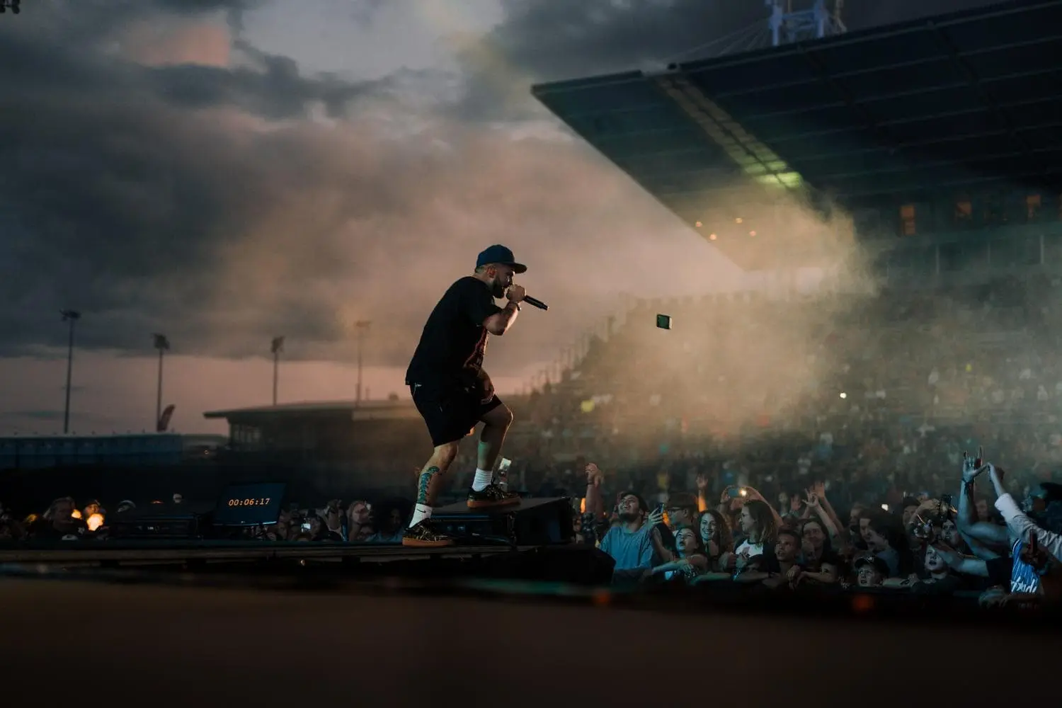 Rapper performs on stage with microphone in front of a cheering crowd at a stadium.