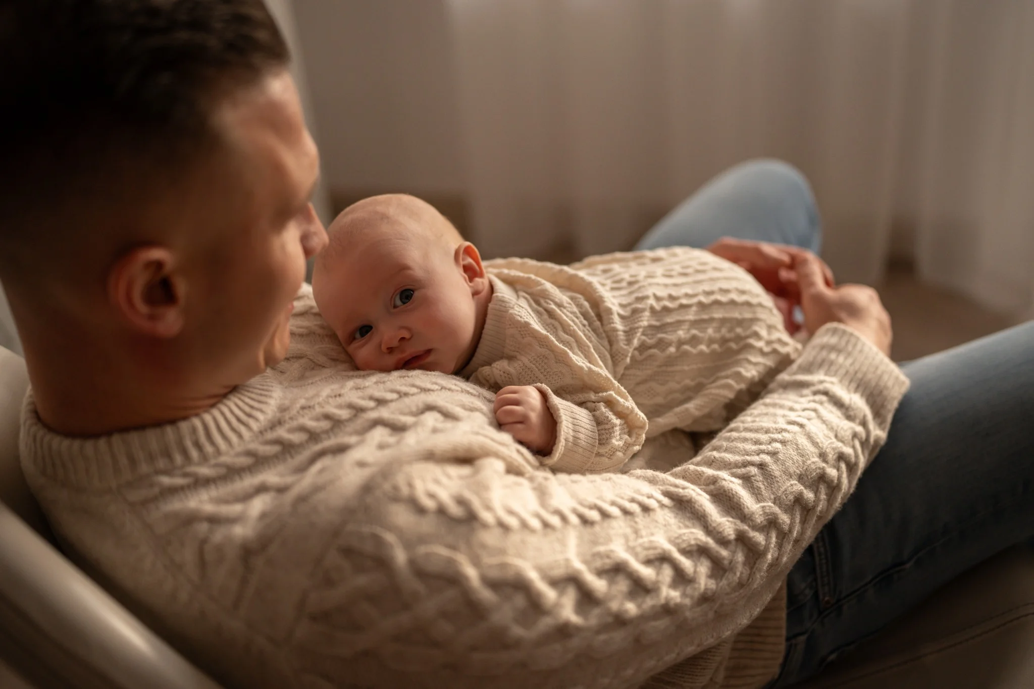  Na zdjęciu widnieje rodzina podczas pikniku na świeżym powietrzu, obok spokojnego jeziora. Składa się z mężczyzny, kobiety i małego dziecka. Mężczyzna ma na sobie jasnoniebieską koszulę i krótkie spodenki, siedzi z przodu i trzyma dziecko na kolanach. Kobieta, ubrana w kolorową sukienkę i kapelusz, siedzi obok i uśmiecha się, patrząc na dziecko. Sceneria jest zielona, z dużą ilością trawy i drzew w tle. Całość tworzy spokojną i sielankową atmosferę.