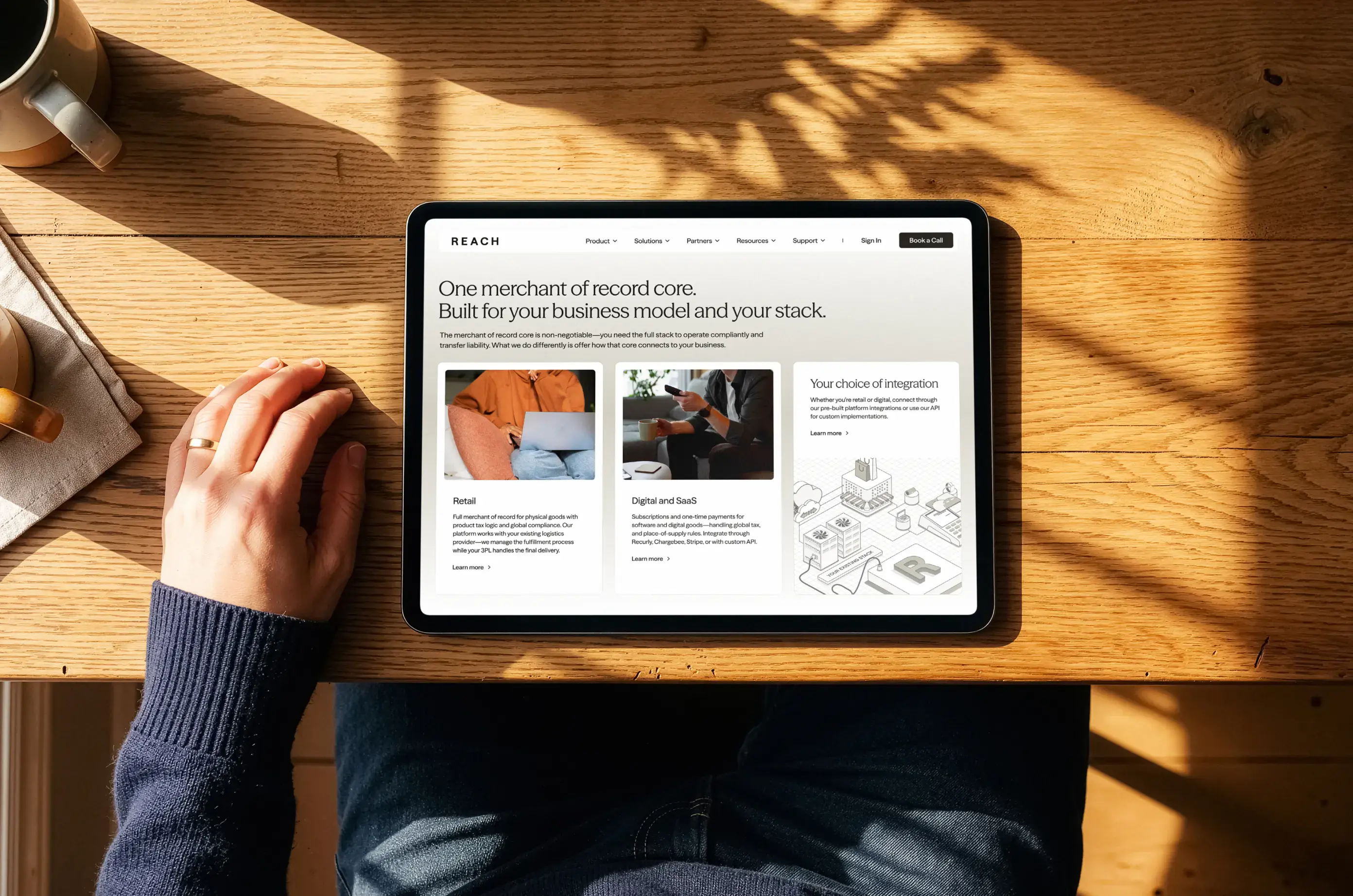 Reach website on a tablet at a sunlit wooden table, showing retail, digital and SaaS, and integration options.