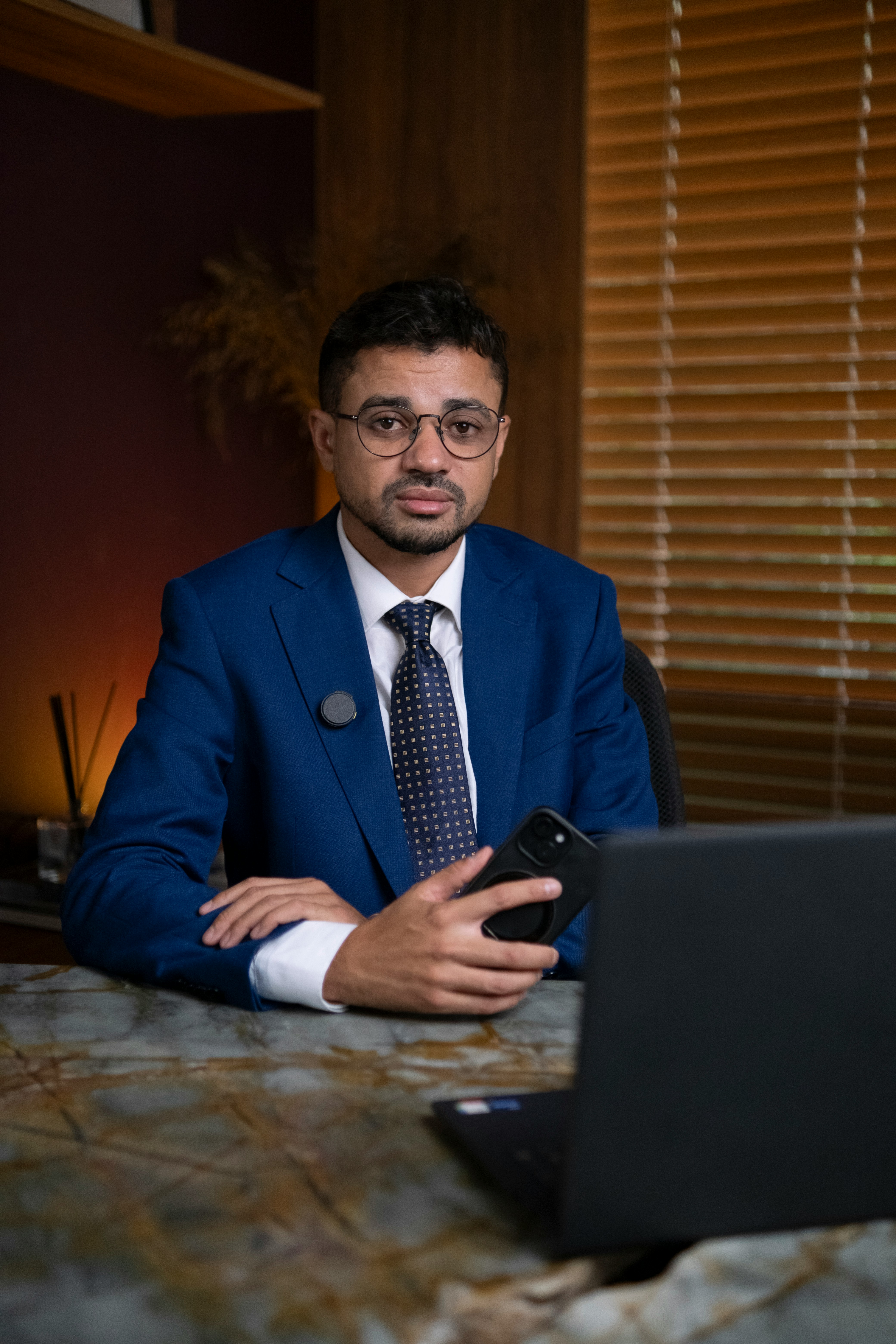 Man in suit holding phone at desk with laptop