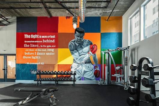 A gym interior featuring a colorful mural and workout equipment, emphasizing fitness and motivation.