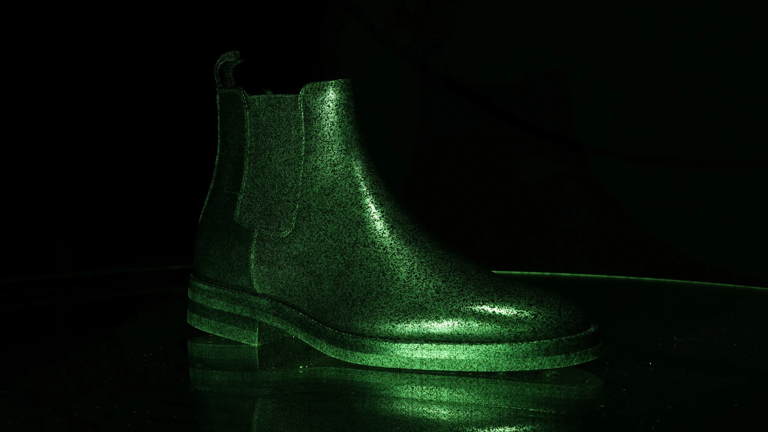 Shiny black leather boot on glass turntable, illuminated with green pattern projection.