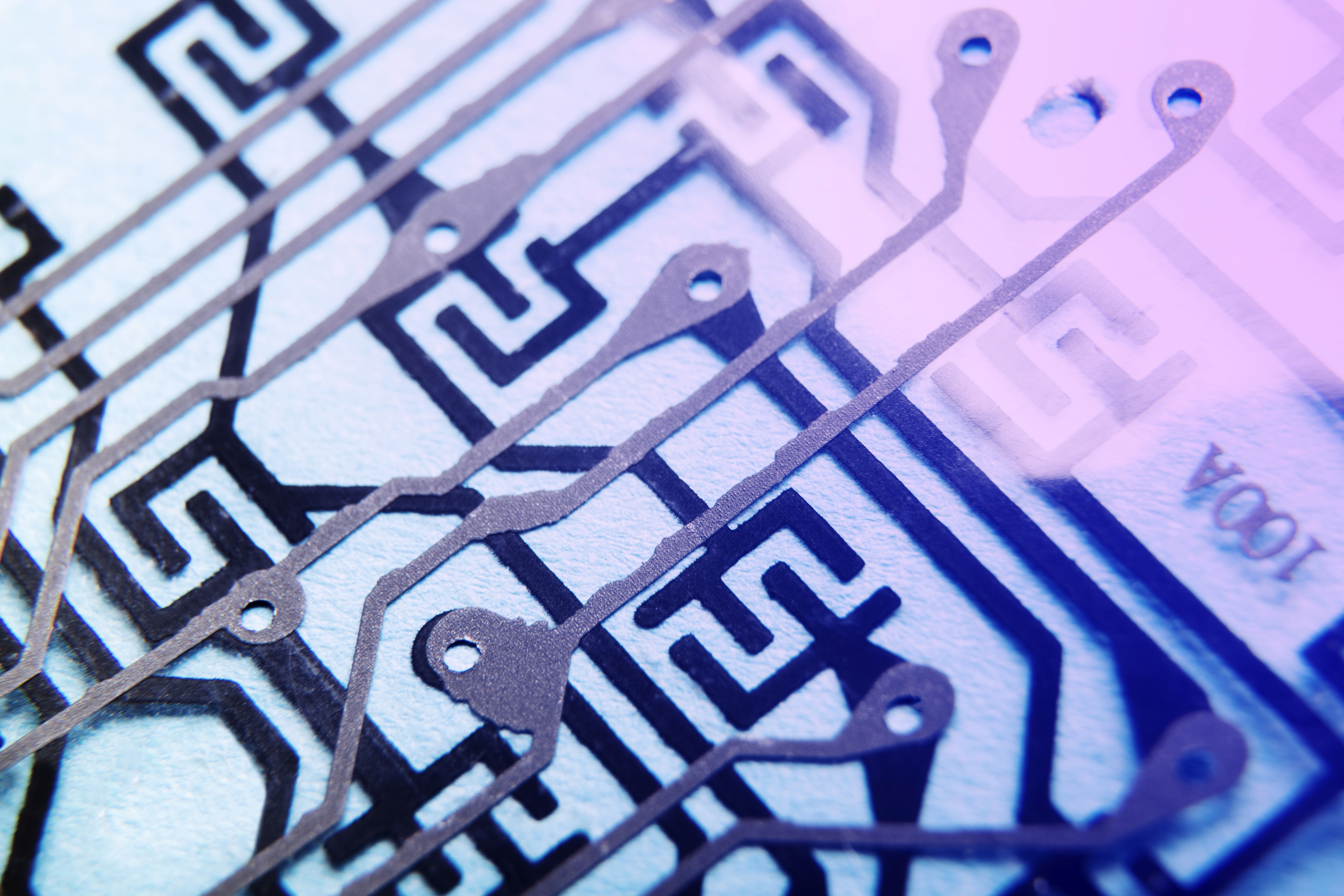 Macro view of printed circuit board traces with cool purple-blue lighting.