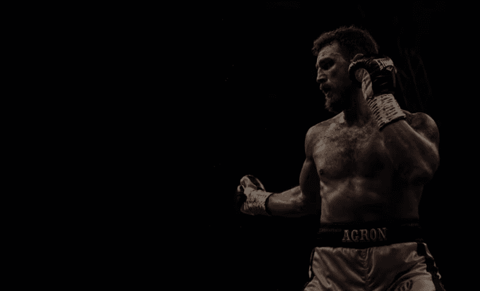 Hero shot of a Agron Smaski boxing coach throwing a focused punch with headline overlay — personal boxing training in Dubai.