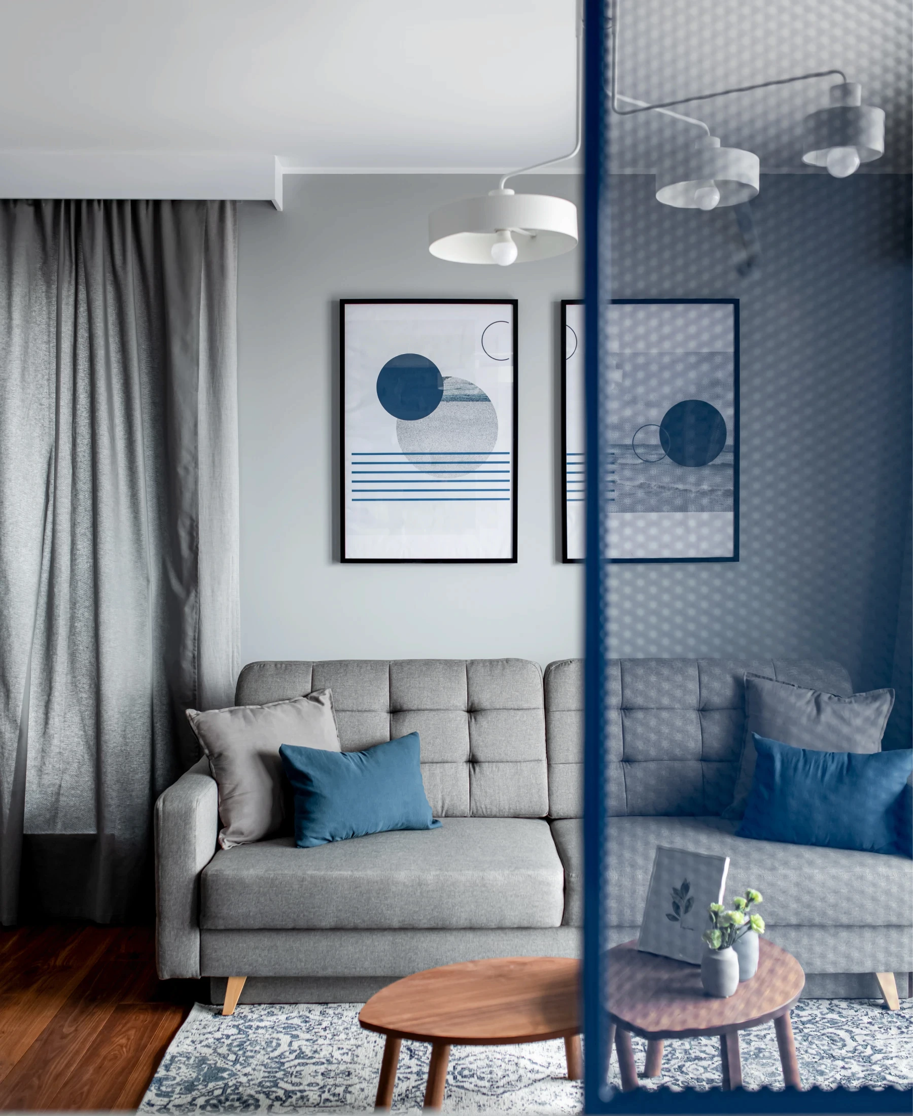 Salon z szarą sofą, designerską szklaną przegrodą oraz niebieskimi akcentami.