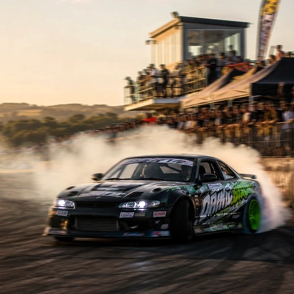 a drift car slides with smoking tires in front of a packed crowd at sunset