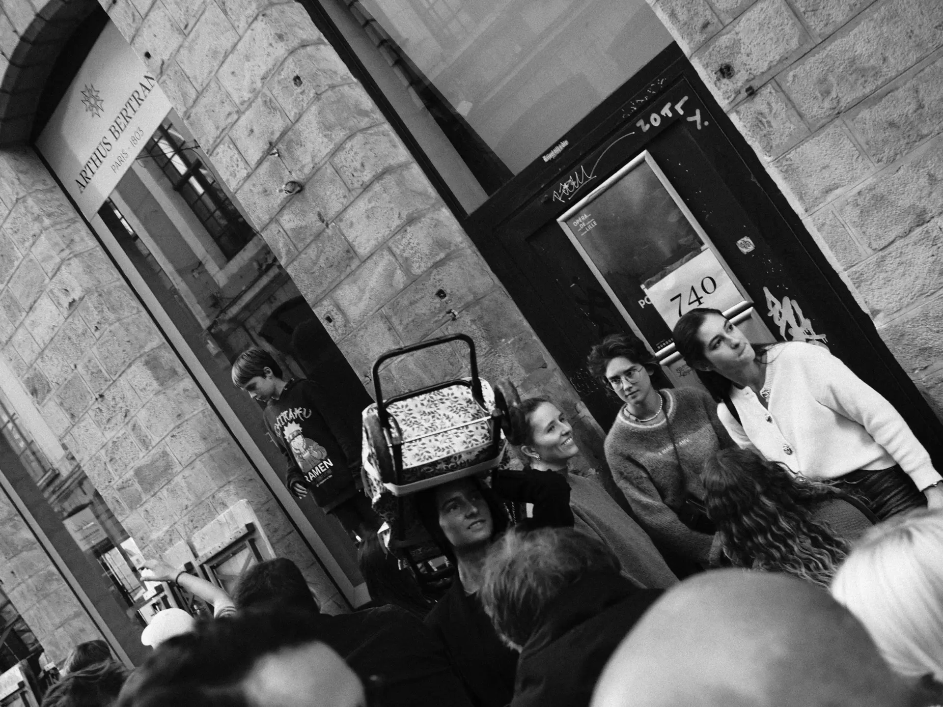 People around a doorway with a stroller full of goods, in black and white
