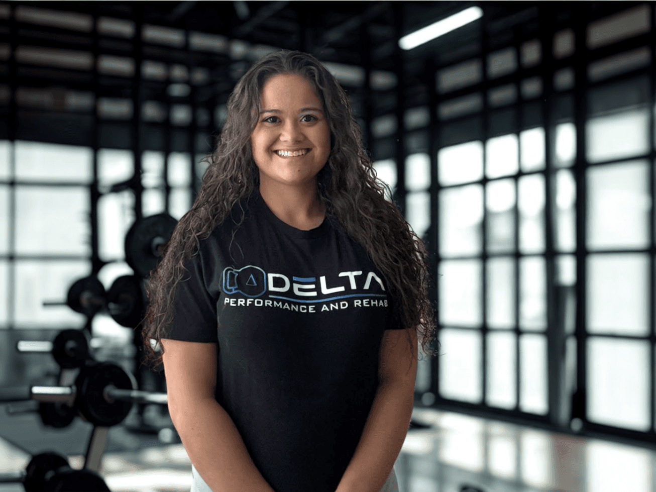 Female team member at Delta Performance and Rehab standing in a strength training gym—representing client care, expert rehabilitation, and athletic support.