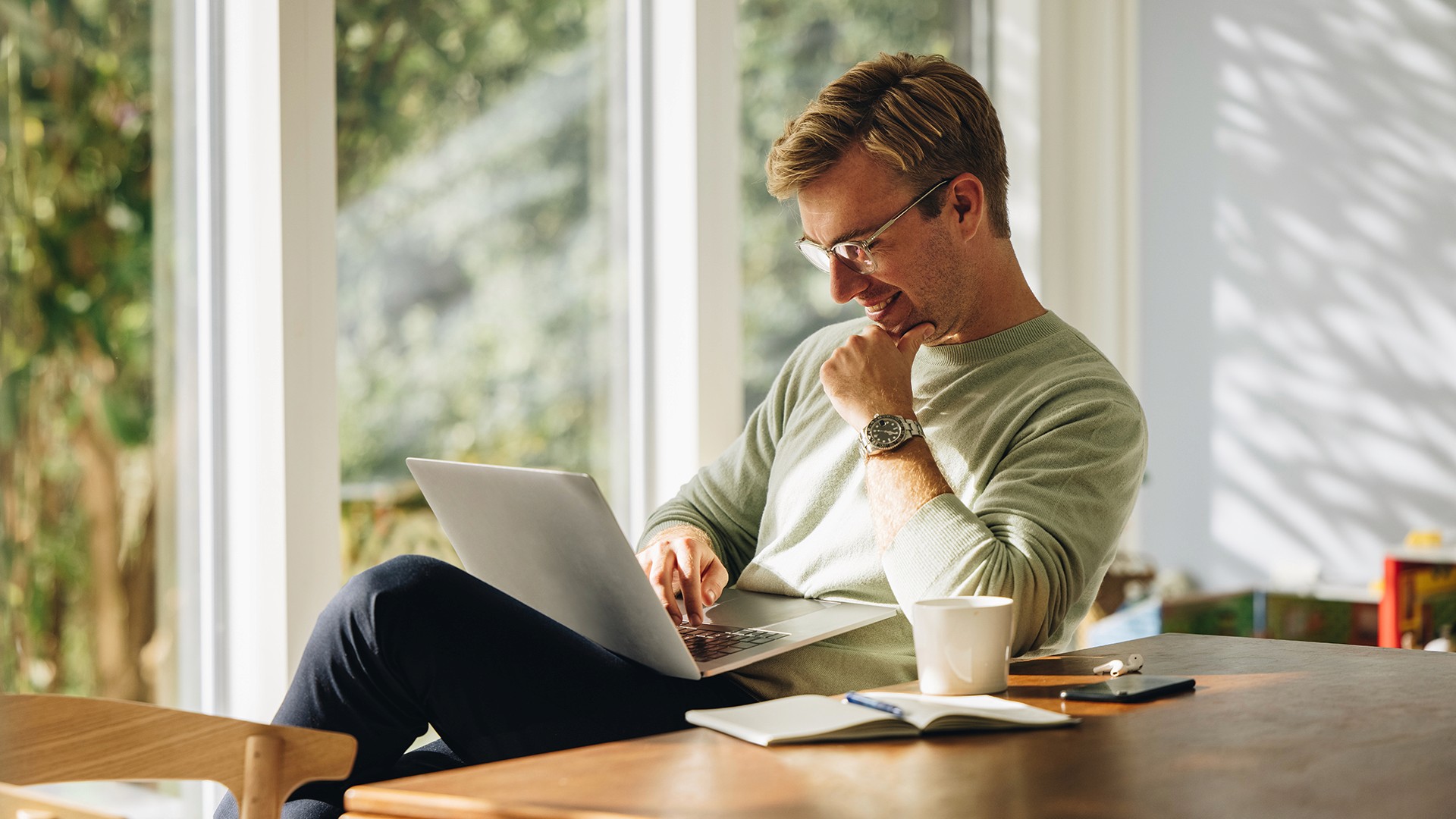 Man working on laptop at table with a garden view
