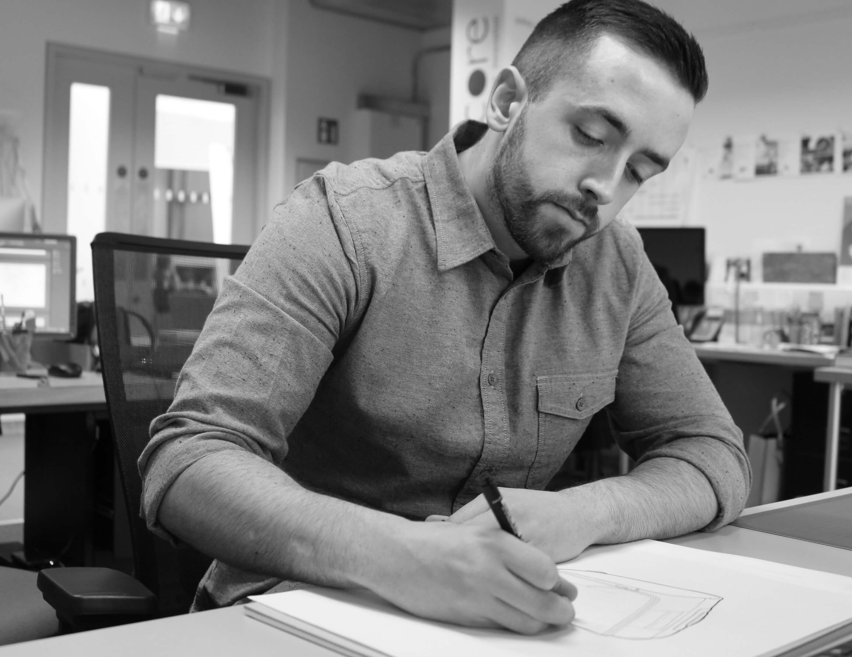 Torso posed shot of cormac looking down and drawing on paper holidng a pen in his right hand