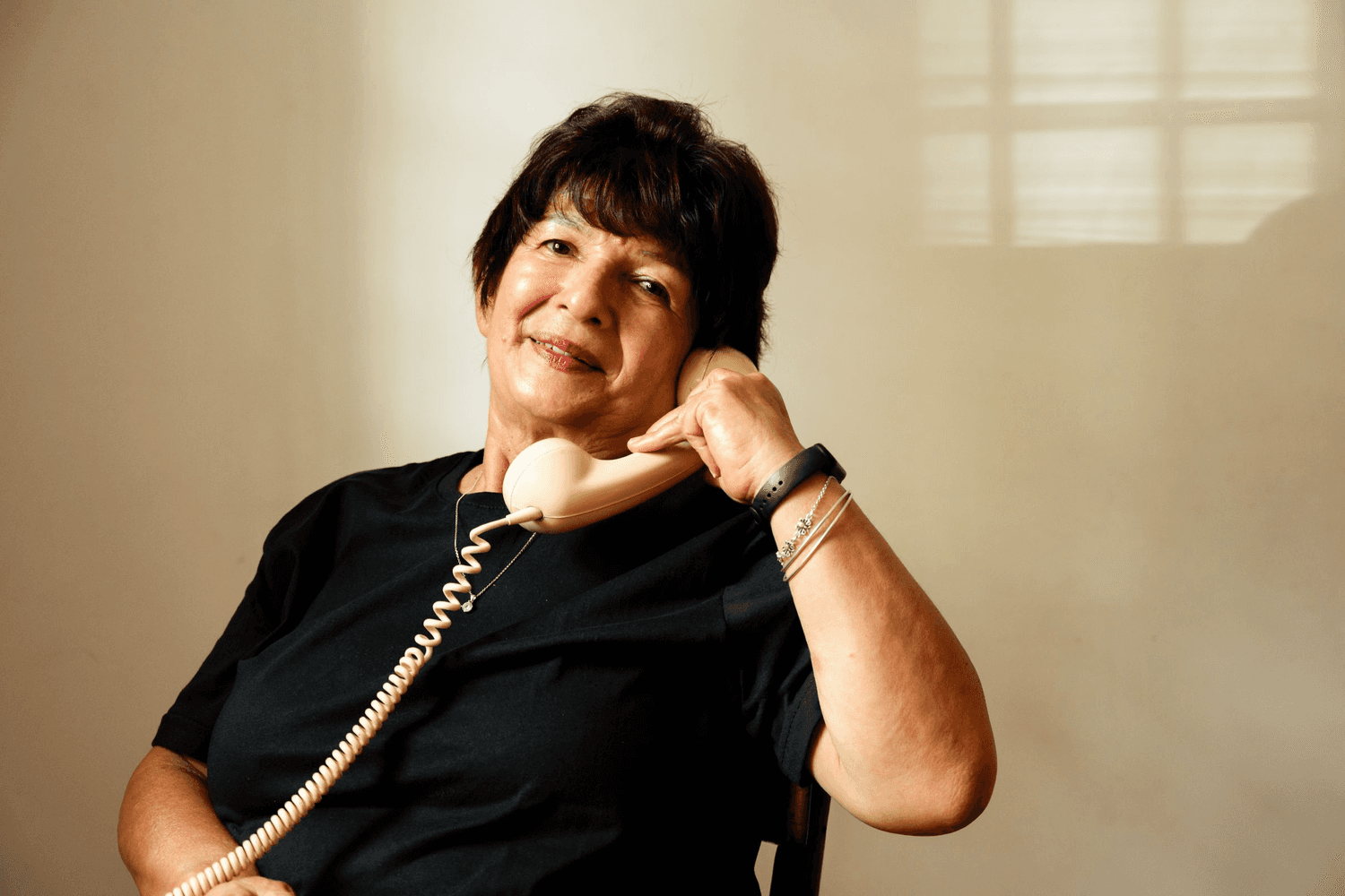 An older woman smiling as she holds a telephone handset to her ear.
