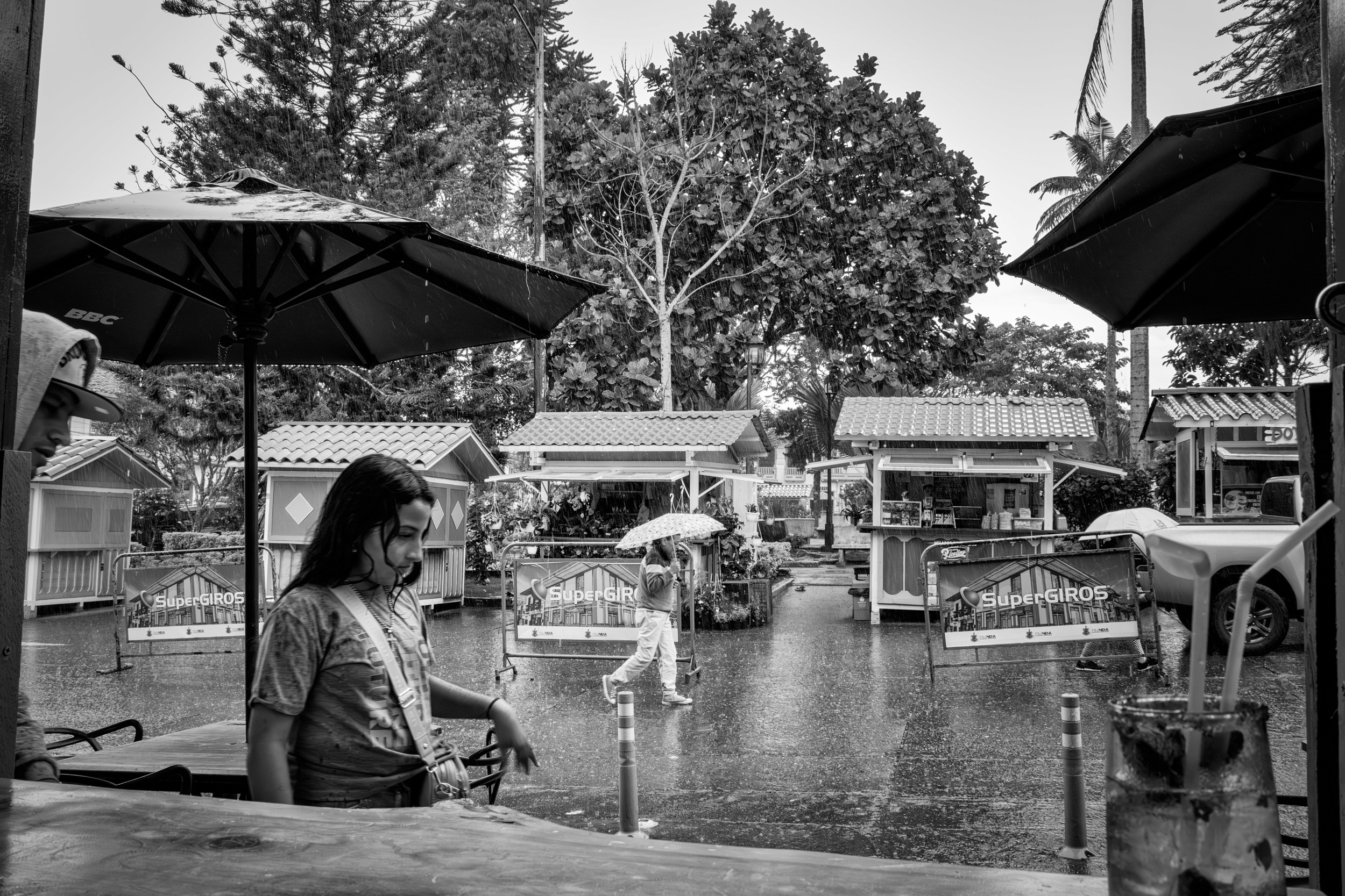 Rainy street scene with people passing by a bar window.