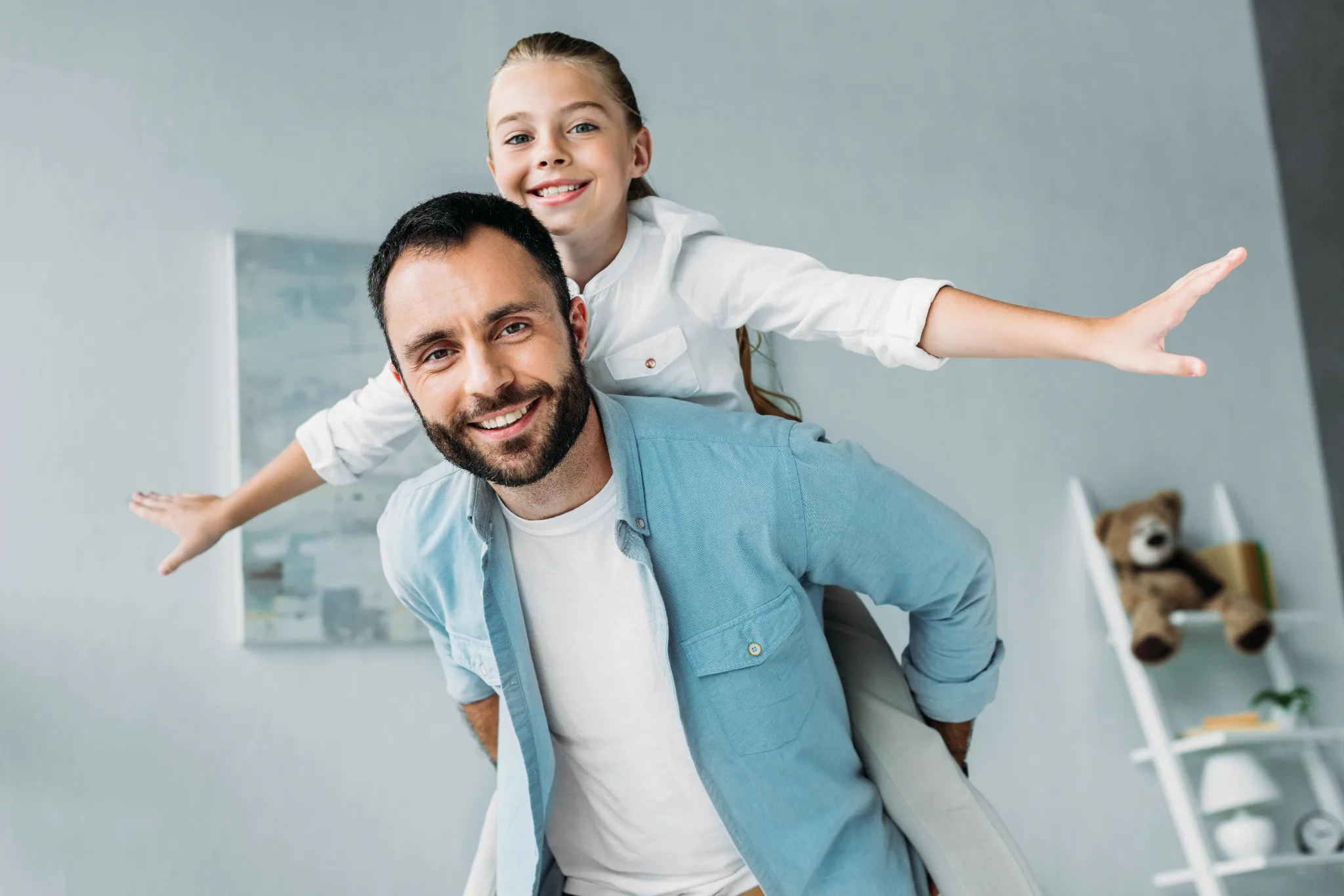 Daughter on her dad's back with her arms spread out like she is flying.