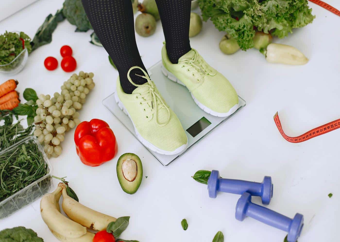 Person standing on scale with veggies, fruits and dumbbells around them to showcase the 5 pillars of health