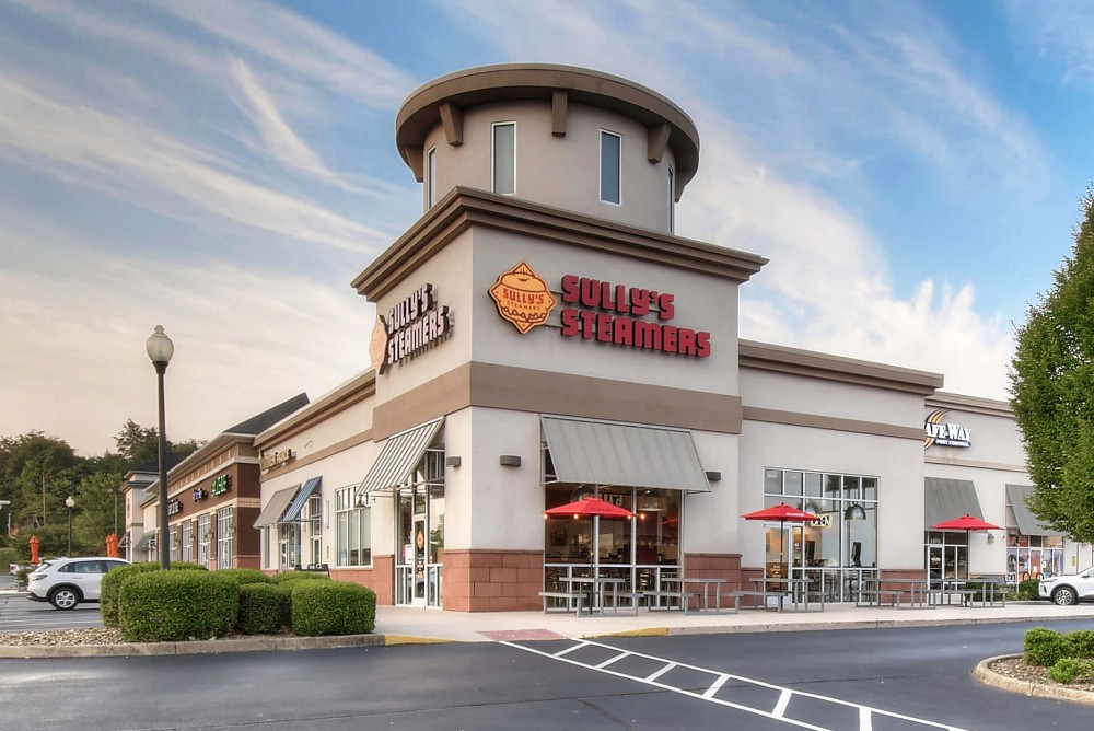 Exterior view of a fast-food restaurant with a round tower, surrounded by green landscaping and blue skies.