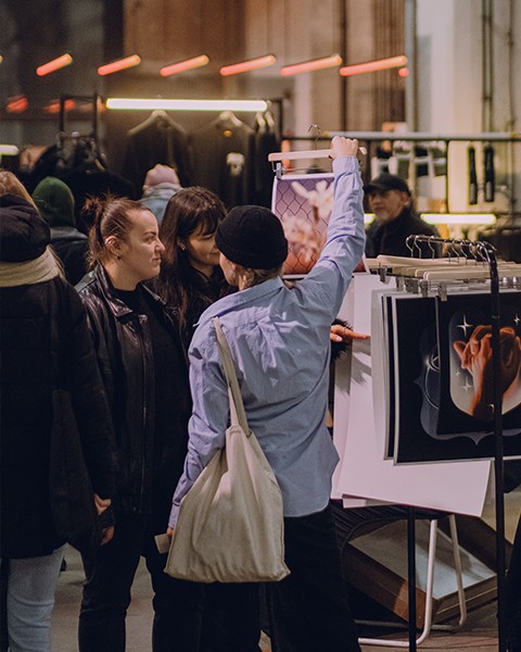 Zdjęcie przedstawiające kilka osób na targach, którzy oglądają plakaty i sztukę.