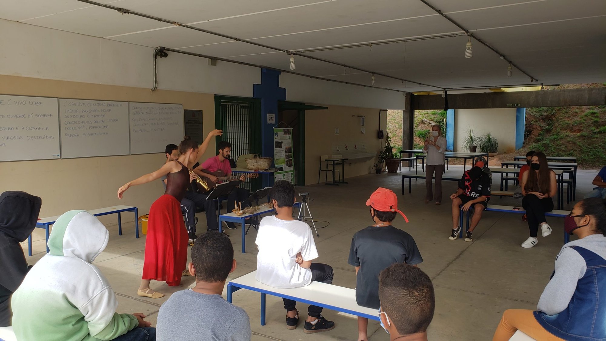 Bailarina de saia vermelha apresenta espetáculo de dança sobre árvores ameaçadas para alunos em pátio de escola