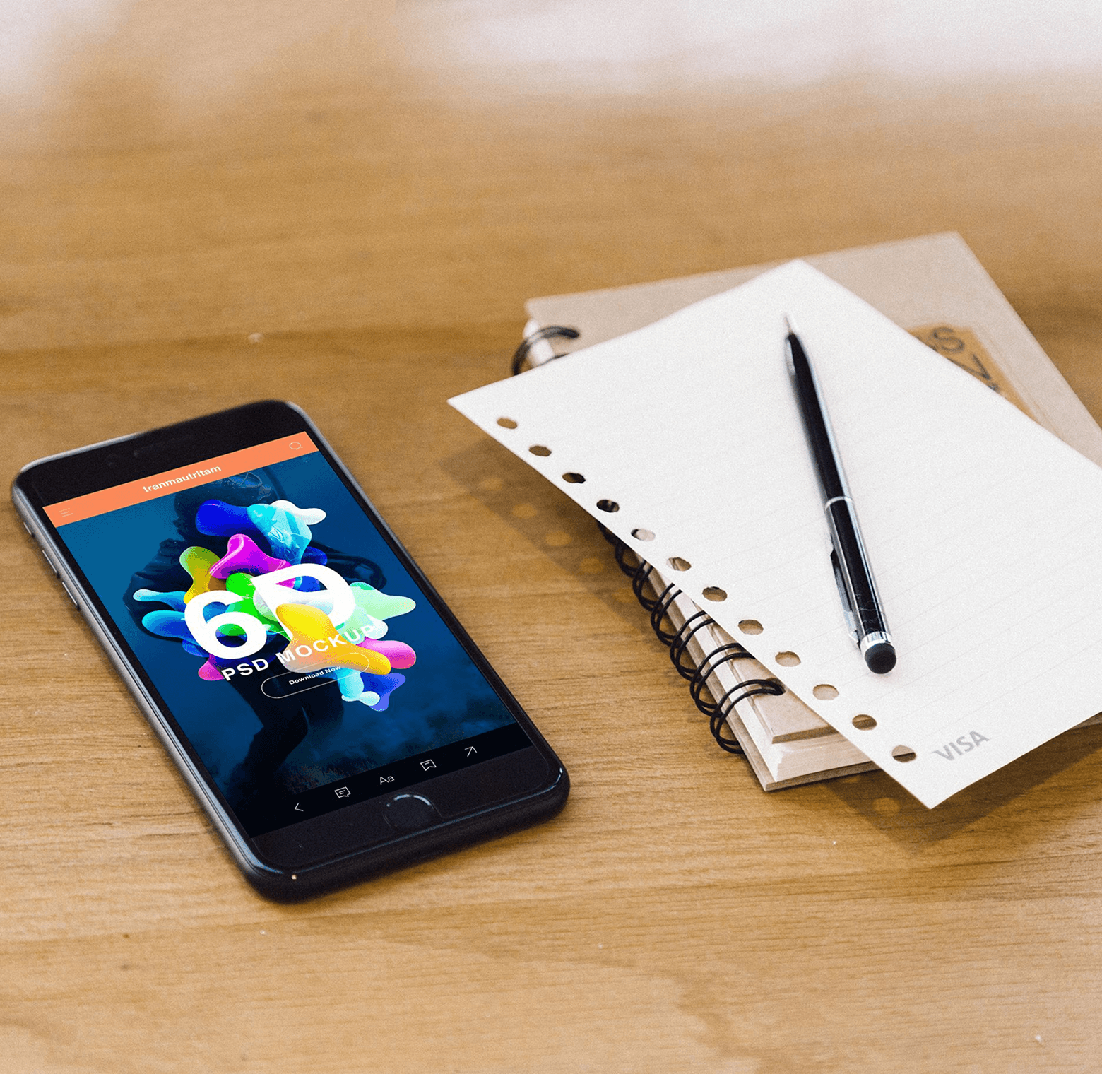 Smartphone with a colorful app screen on a wooden desk beside a spiral notebook and pen