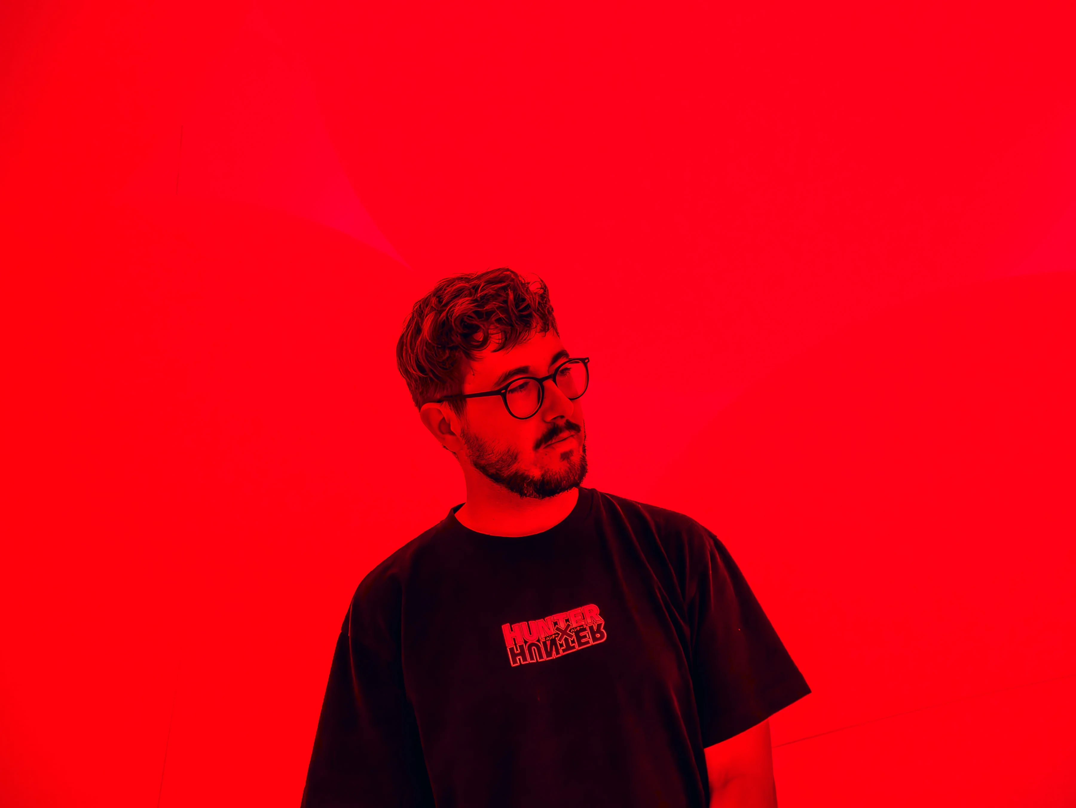 Ismael Casado with glasses and a black t-shirt stands in front of a red background.