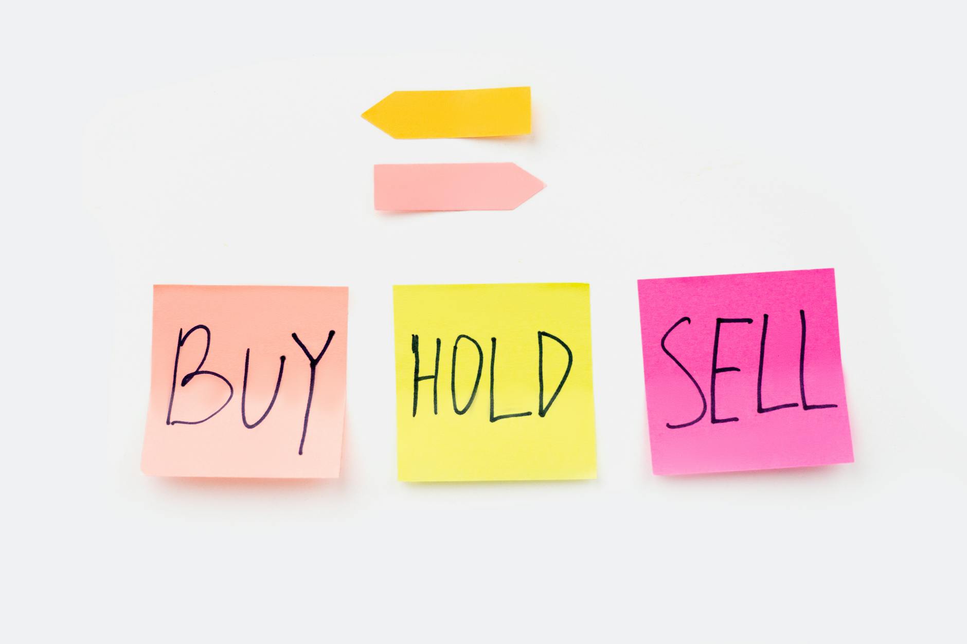 Three colorful sticky notes on a white surface, each handwritten in black marker with the words "BUY" (pink), "HOLD" (yellow), and "SELL" (pink), representing property investment decision options.