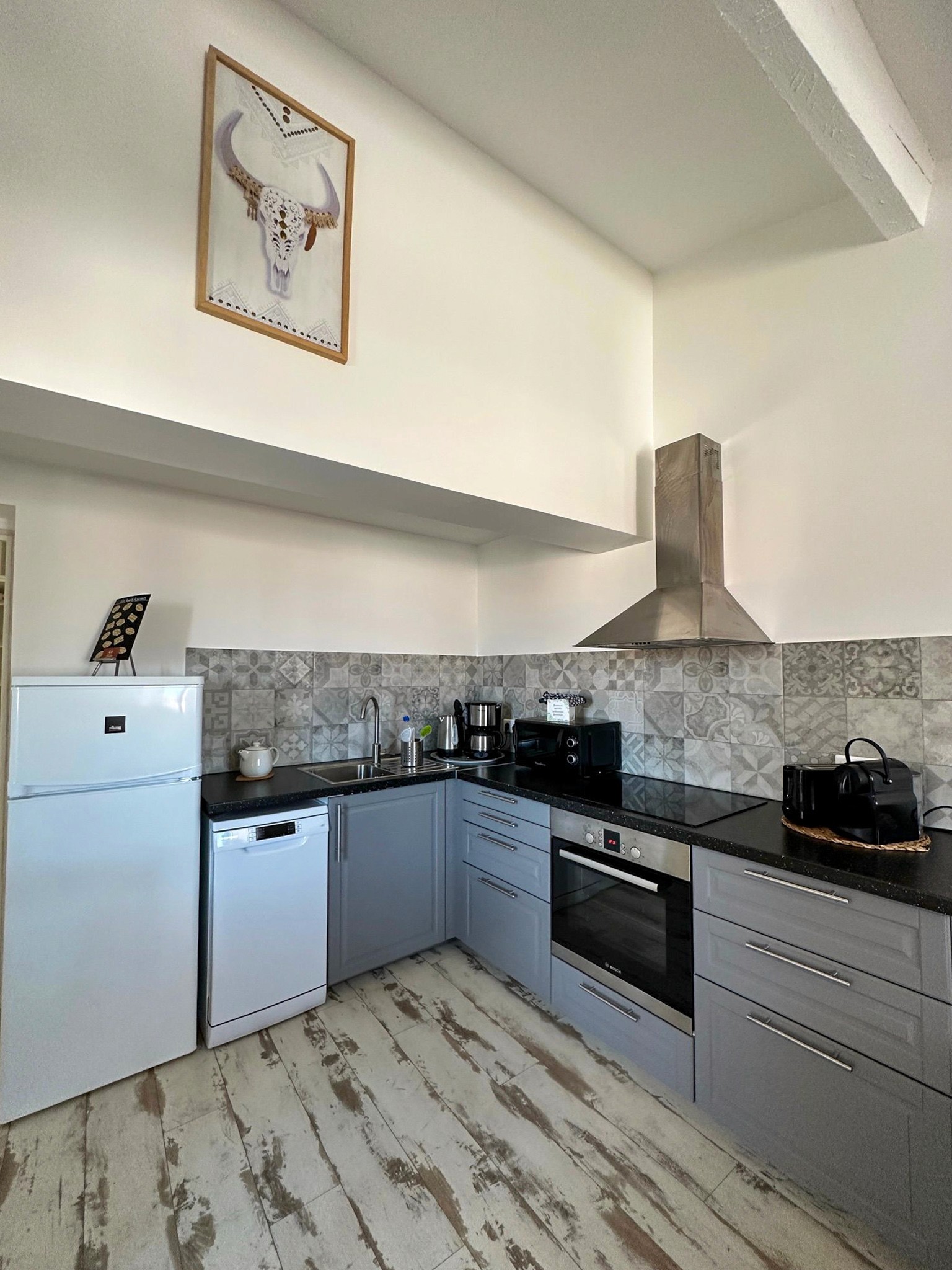 Petite cuisine équipée blanche et bois moderne avec électroménager complet et éclairage sous meuble.