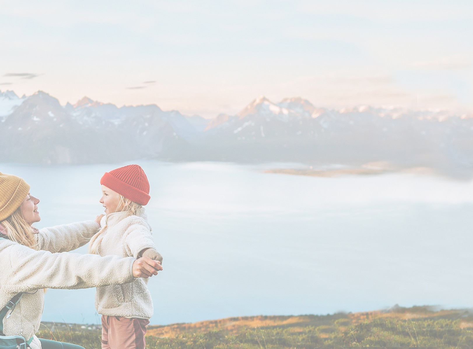 Mother and daughter outdoors, hiking near a large lake with mountains in the background.