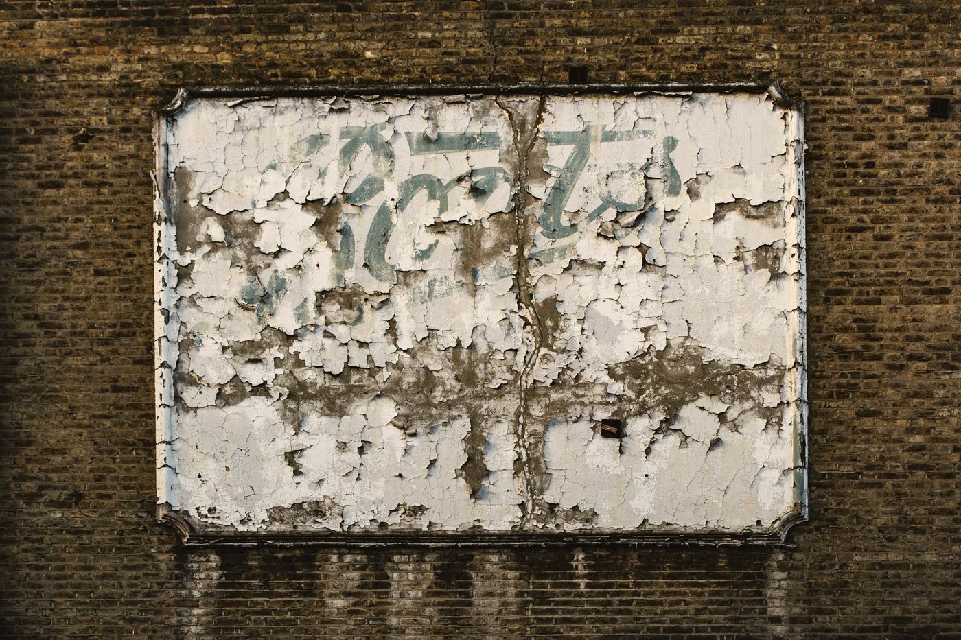 A white enamel sign on a brick wall, its paint chipped and its lettering worn away
