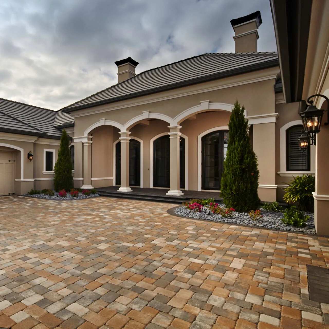 A welcoming motor court Warm-toned interlocking paver driveway in front of a home with an arched porch.