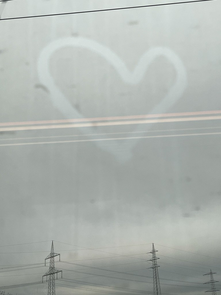 "Heart drawn on a window with gray, cloudy sky in the background"