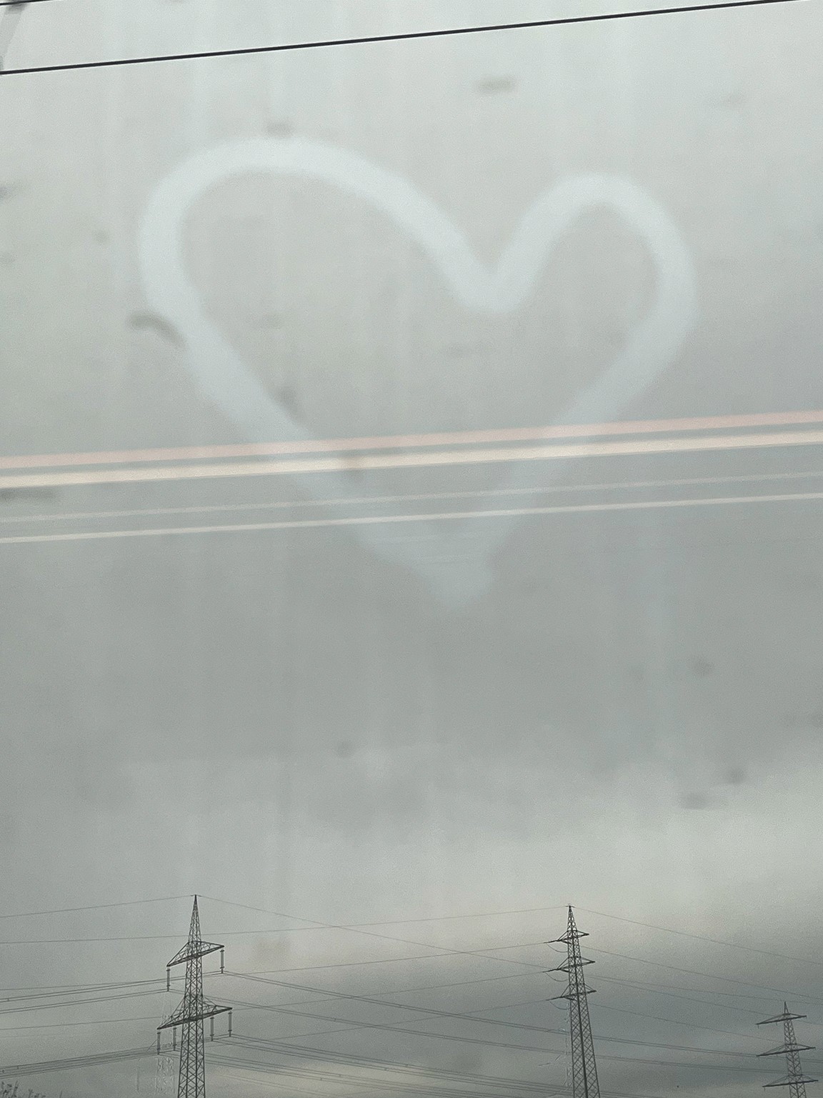 "Heart drawn on a window with gray, cloudy sky in the background"