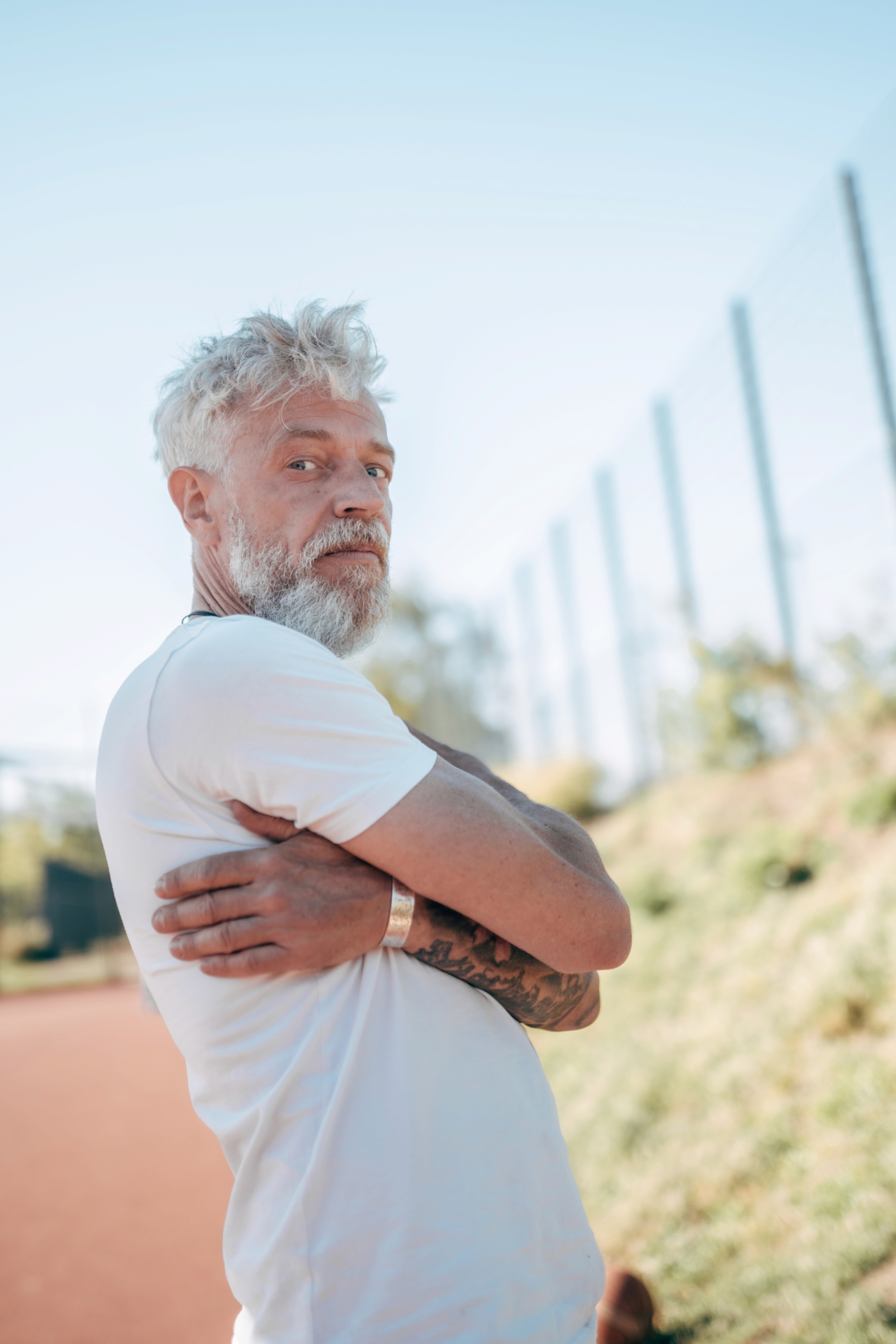 älterer Mann im besten Alter stehend seitlich die Arme verschränkt blauer Himmel
