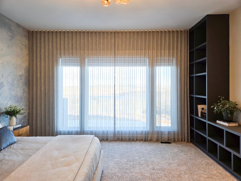 Image of Luxurious primary suite with plush bedding, custom window coverings, and modern built-in furniture by KHD Homes.