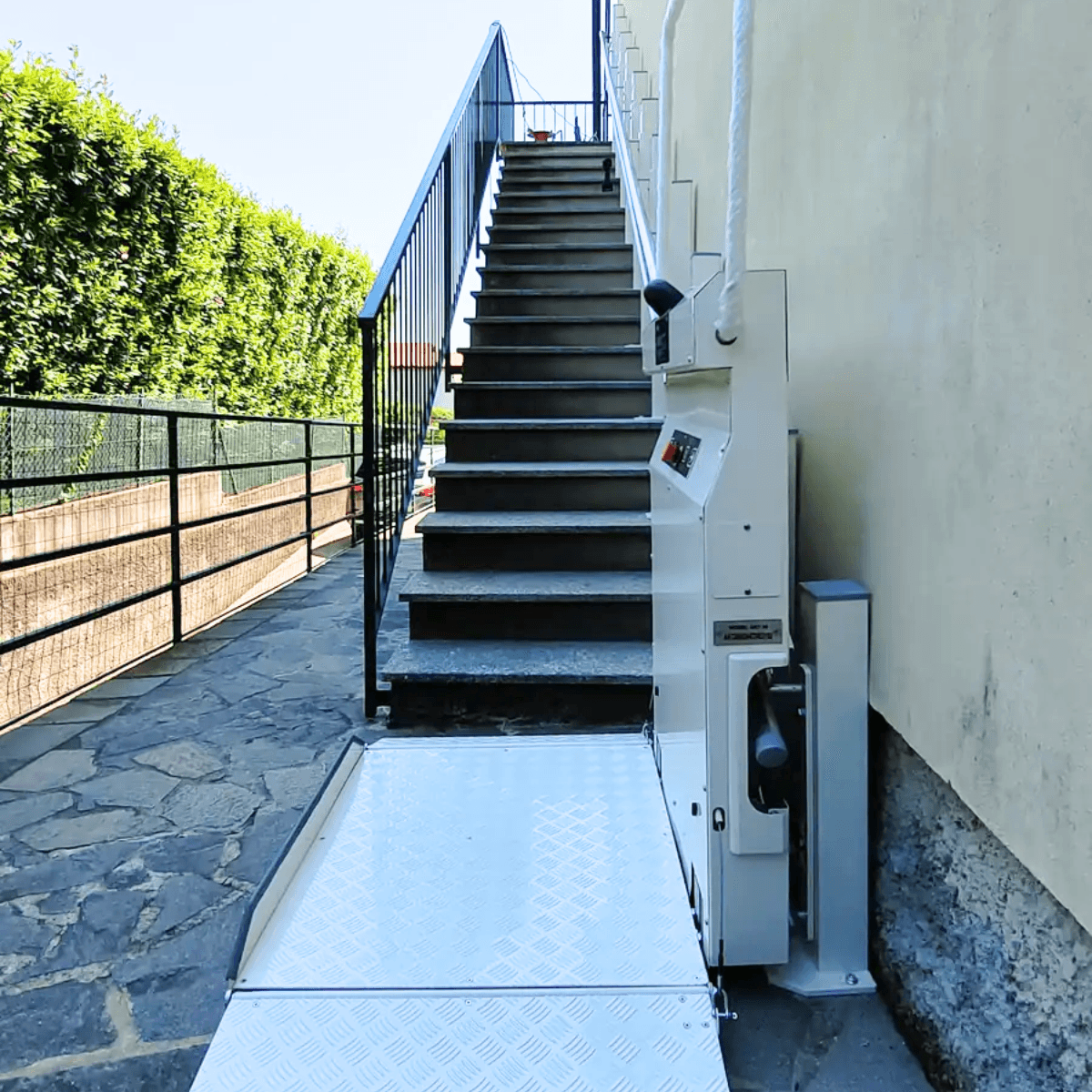 Outdoor incline platform stairlift with folded aluminium platform installed alongside external stone steps at a residential property