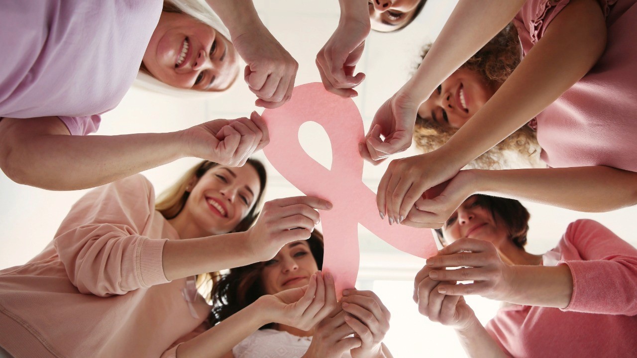 Women in a circle looking down holding a breast cancer ribbon