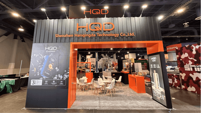 HQD CHAMPS Las Vegas 2025 July 20x20 booth entry view with branded header wall, orange frame structure, and front-facing product presentation