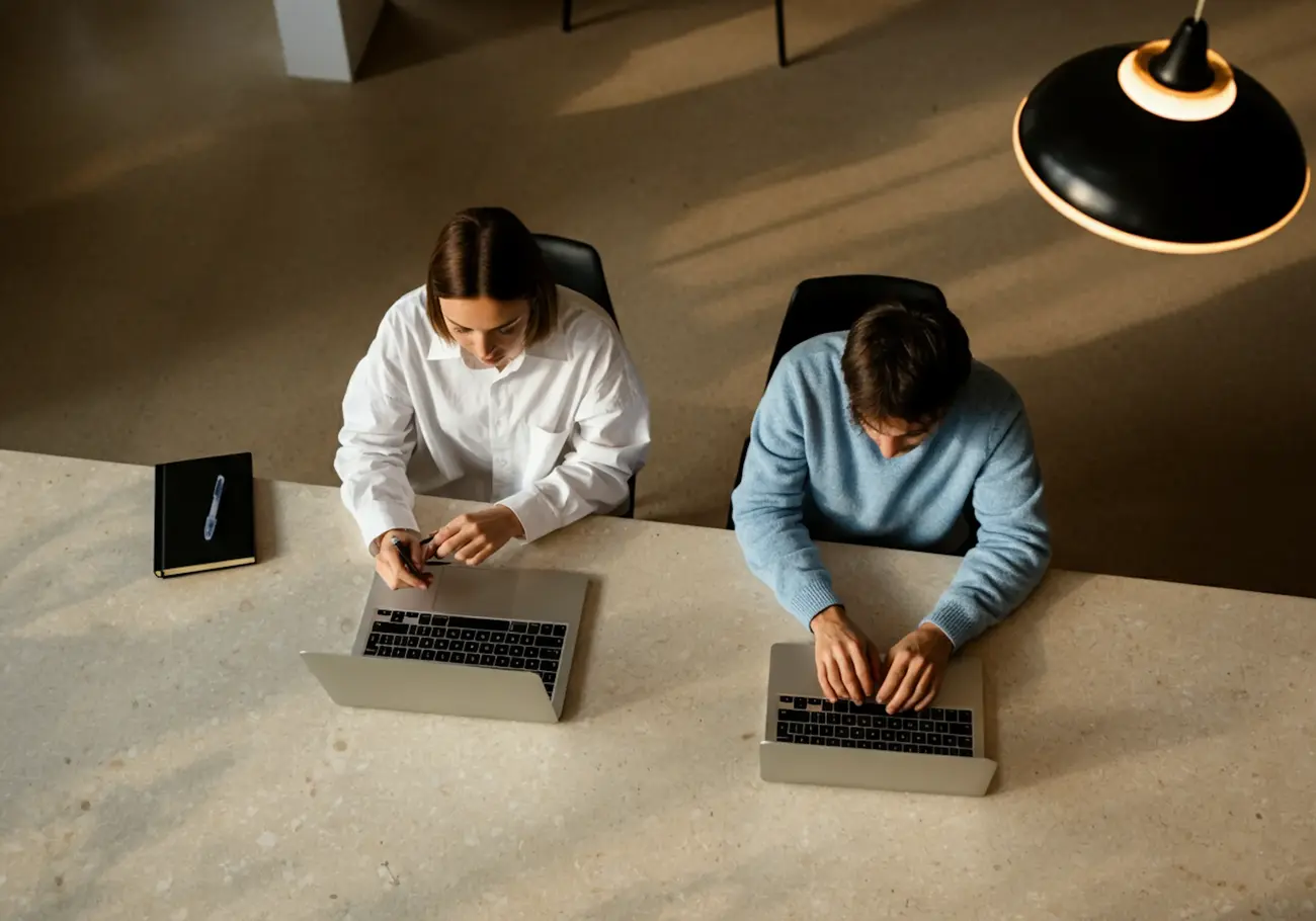Man and woman working side by side at a desk, both focused on their laptops.