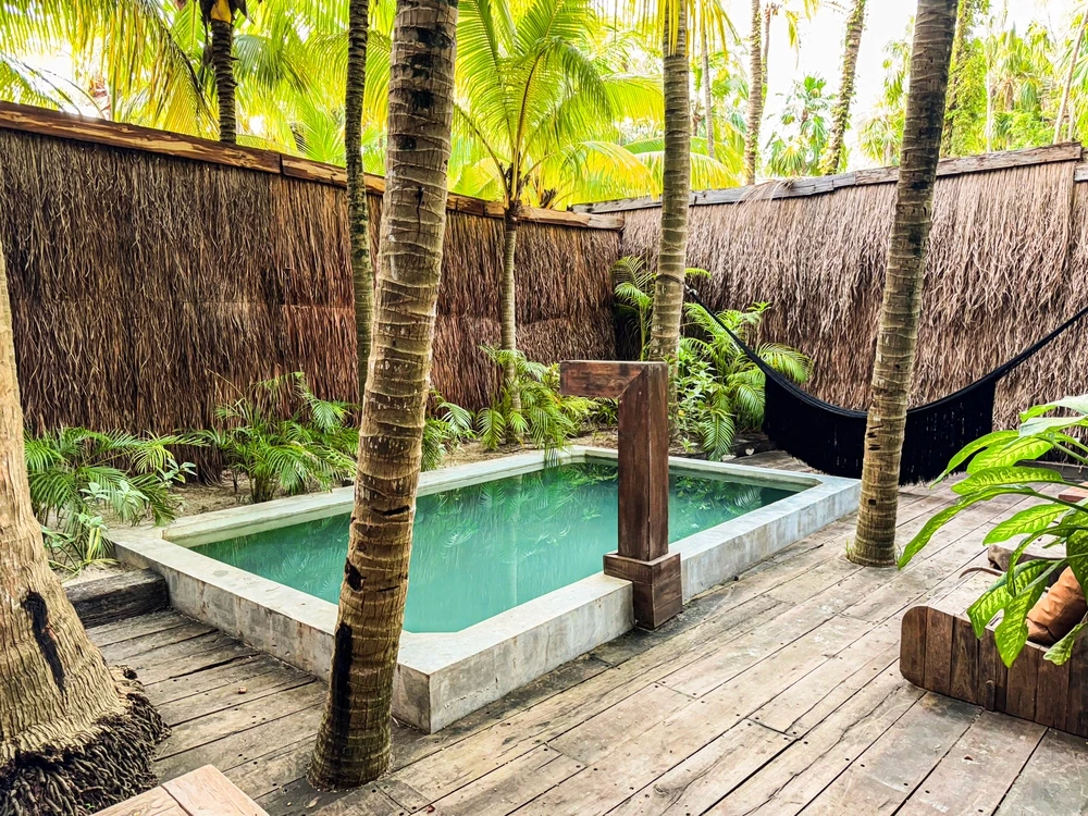 Two Bedroom Villa with Pool at Nômade Tulum showing part of the bed, 2 chairs, decorative furniture, and 2 large windows with jungle view.