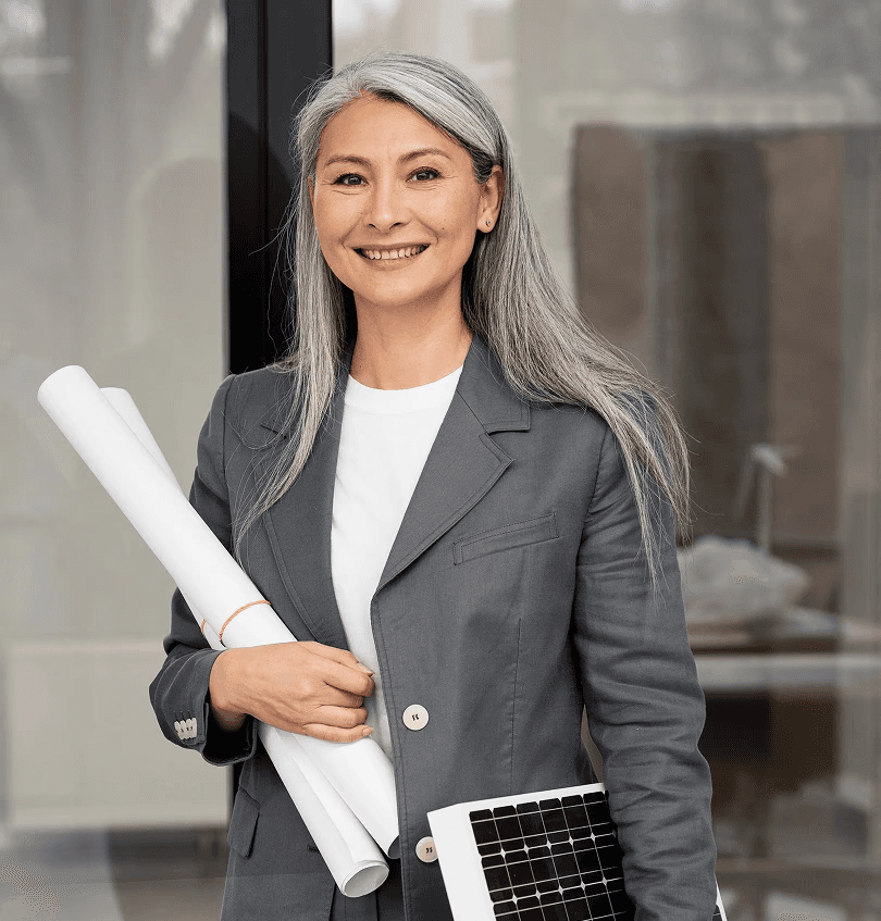 Smiling woman with long gray hair holds rolled blueprints and a solar panel. She's wearing a gray suit, conveying professionalism and eco-focus.
