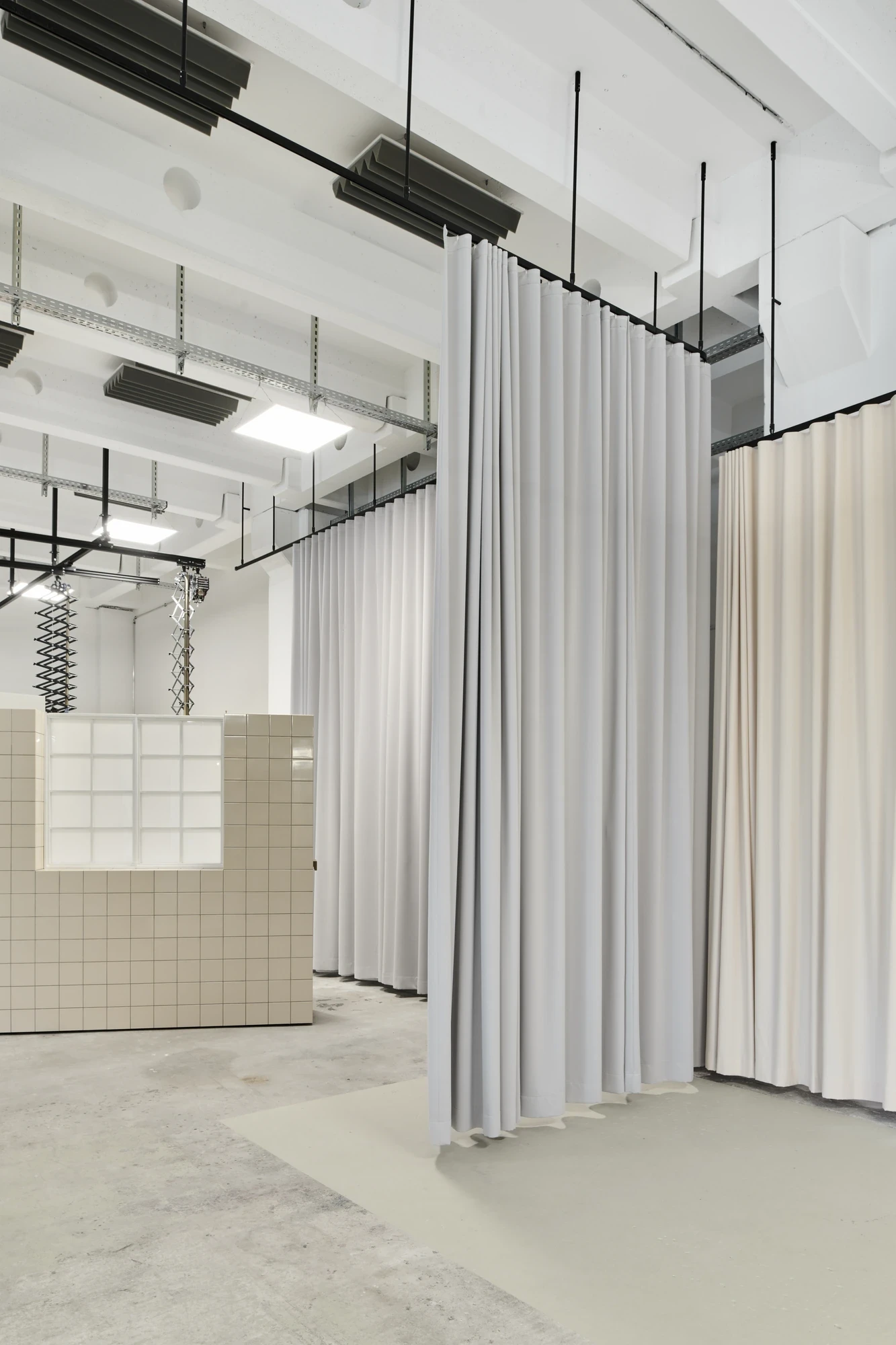 Open interior space divided by suspended grey fabric curtains with a beige-tiled counter and exposed industrial ceiling.