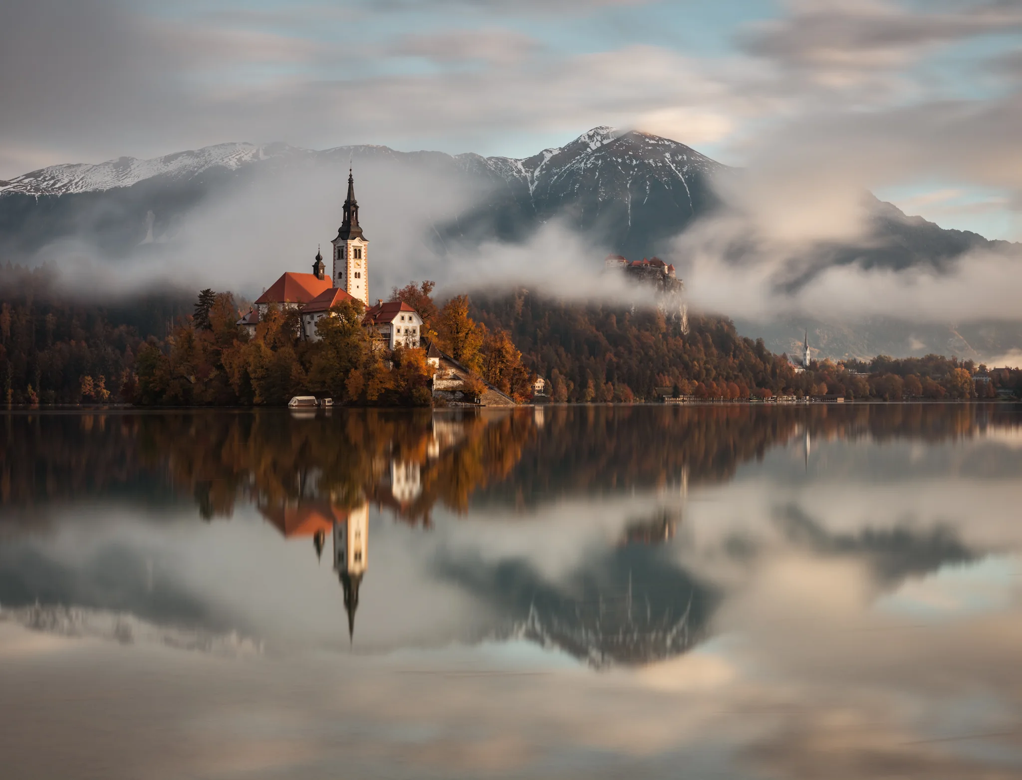Lake Bled, Slovenia, featuring the island church and its mirror reflection on a calm, misty morning with the Julian Alps in the background.