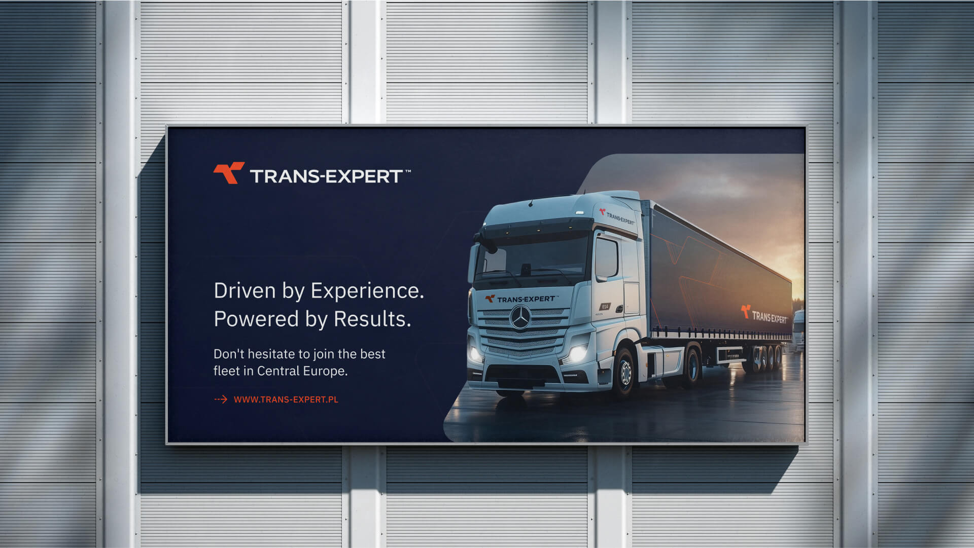 A nighttime digital billboard advertising TRANS-EXPERT logistics company. The billboard features a modern white semi-truck with a dark trailer set against a dramatic, dark sky. Text on the left reads: "Driven by Experience. Powered by Results. Don't hesitate to join the best fleet in Central Europe." Below that is the website: "WWW.TRANS-EXPERT.PL". The billboard is mounted on a modern, ribbed metallic building exterior.