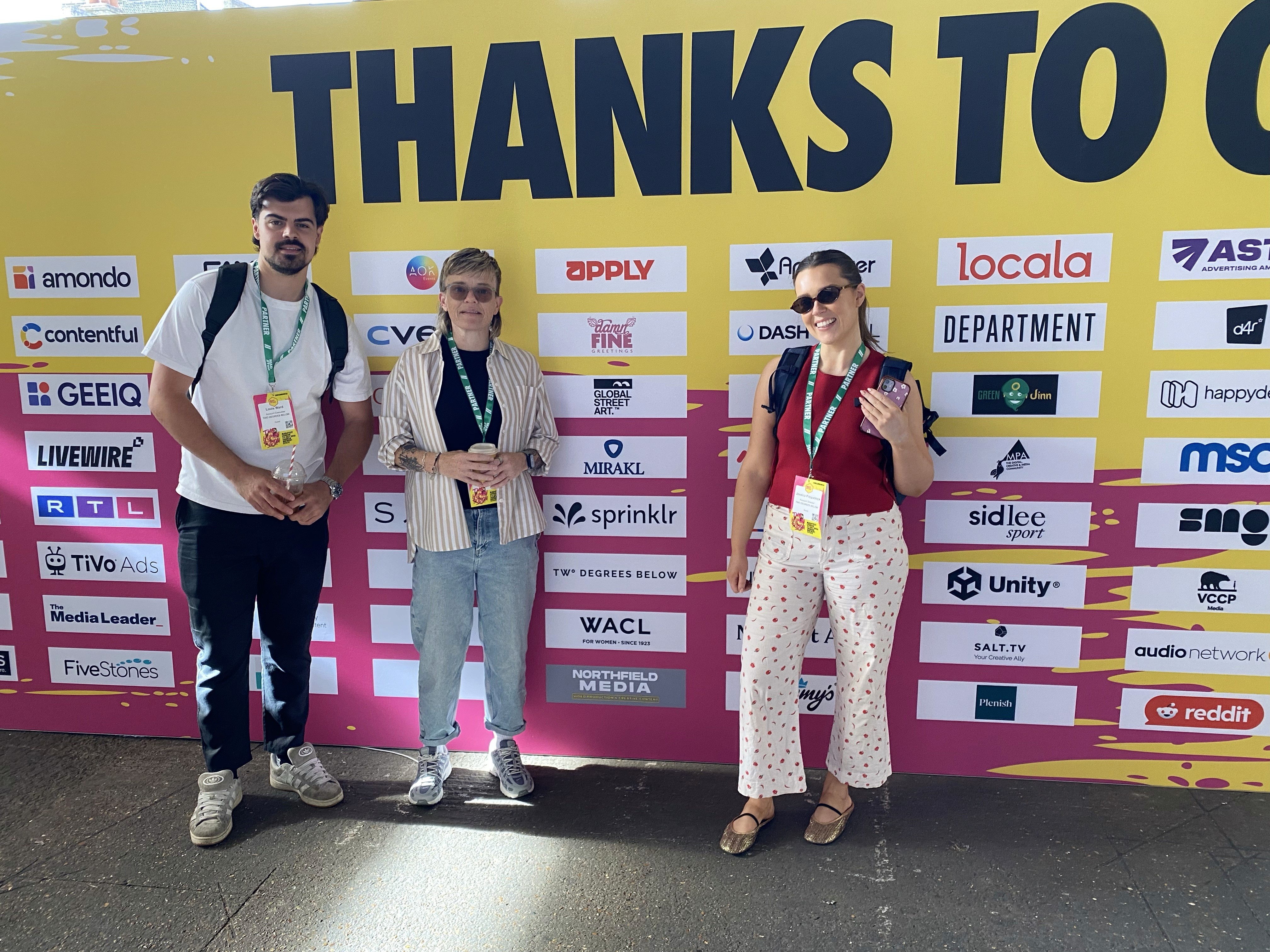 Three members of the Two Degrees Below team pose in front of a yellow and pink sponsor wall at MADFEST 2026