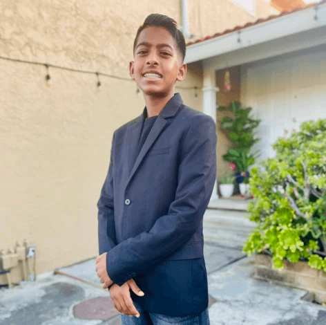 A young person with long, wavy hair sits in front of a plain background, looking directly at the camera.