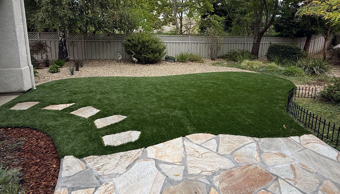 Roseville backyard landscape design with artificial turf, flagstone stepping stones, and a gravel garden bed.