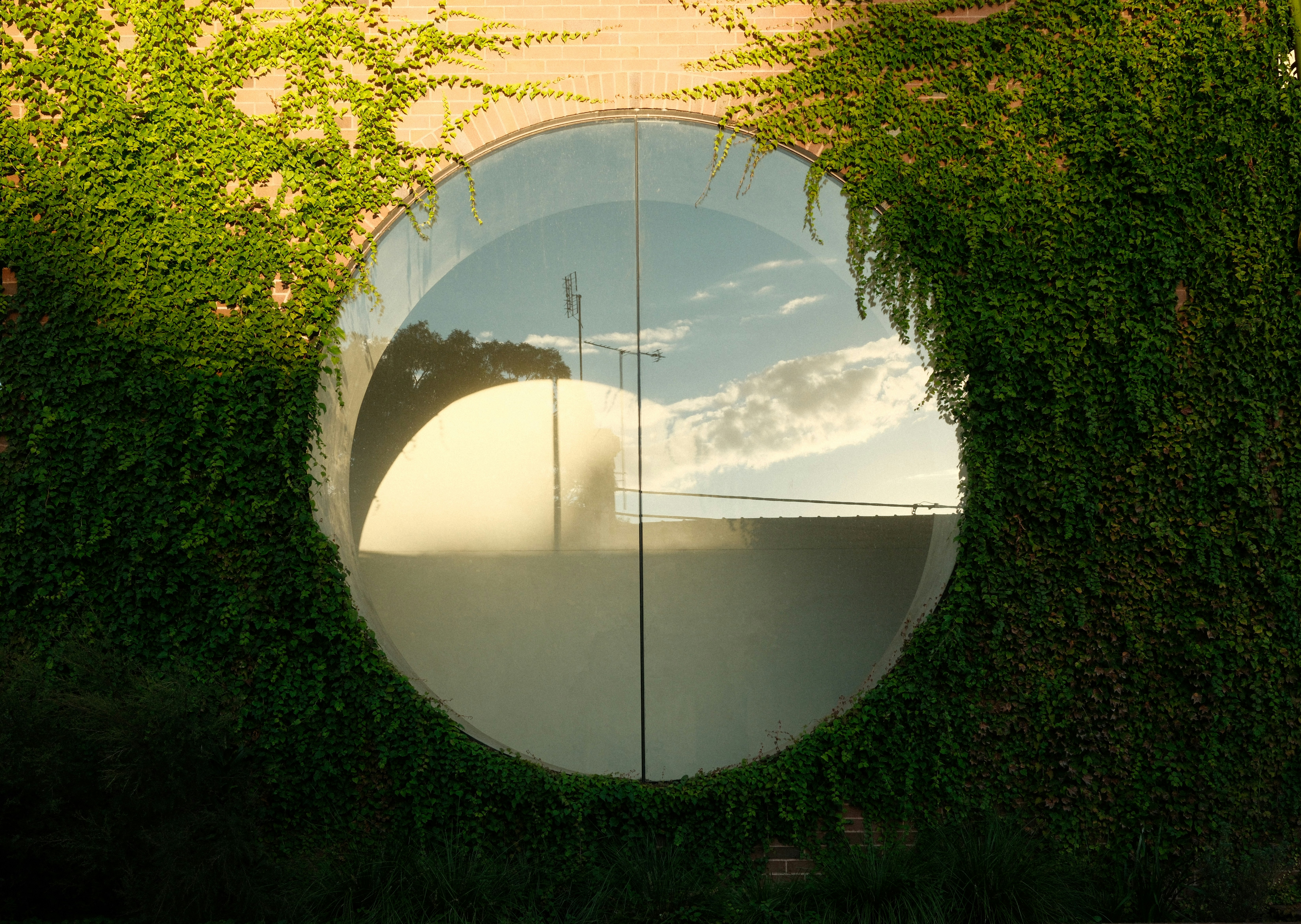 Circular window reflecting sky and trees on brick wall