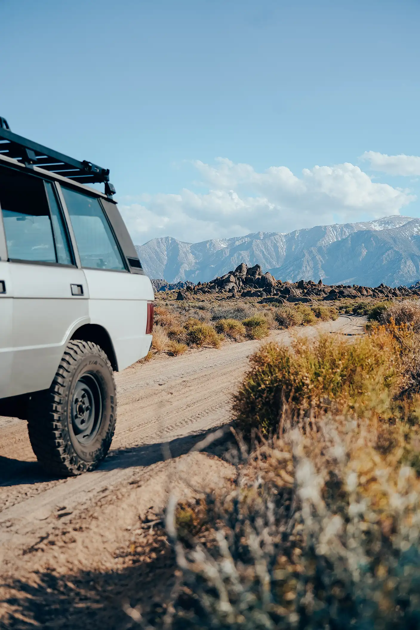 A silver Range Rover SUV on a dirt road with mountains in the distance.