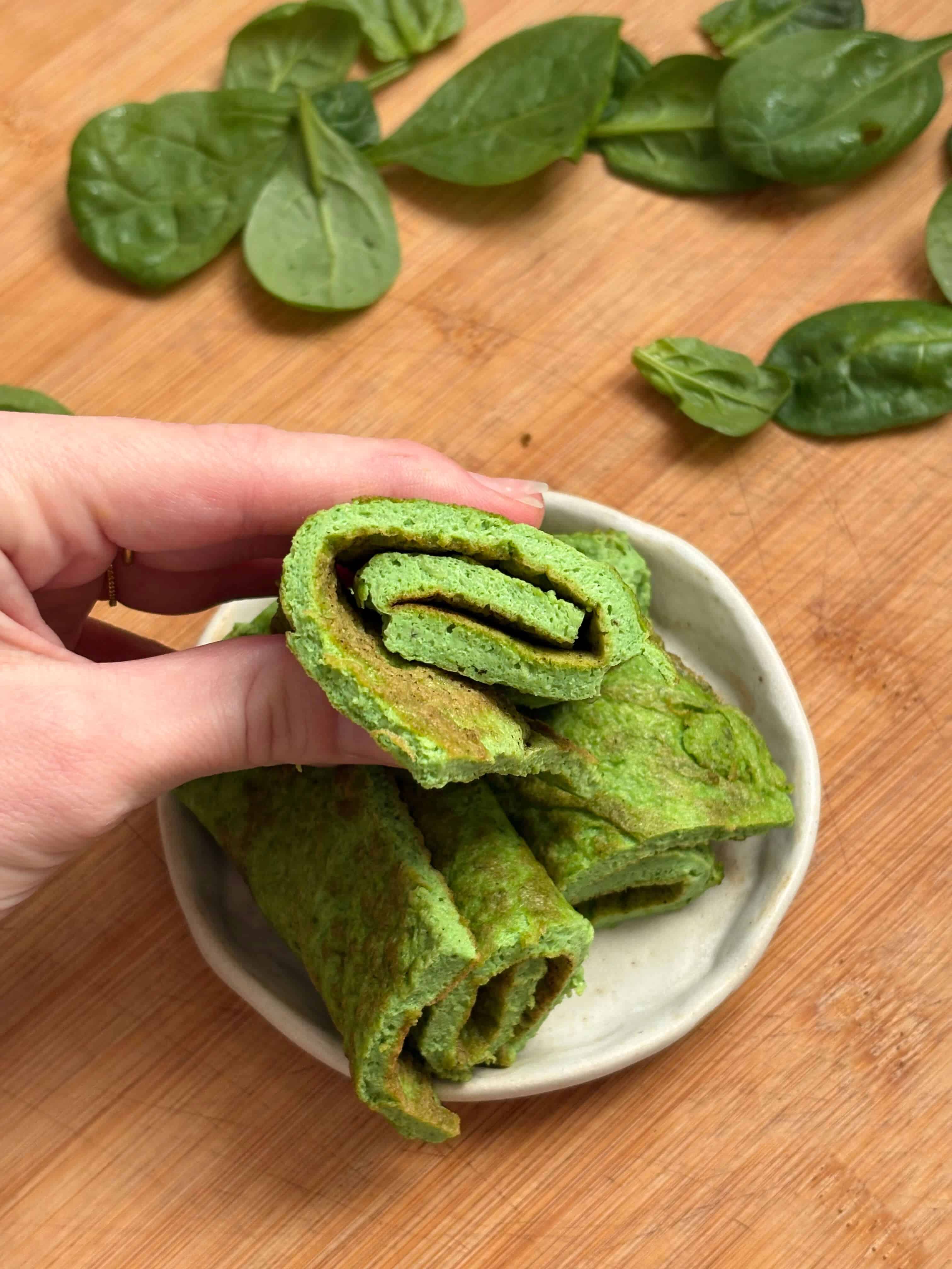 Rolled green egg omelette slices stacked on a small plate, shown as a protein-rich lunchbox option for kids.