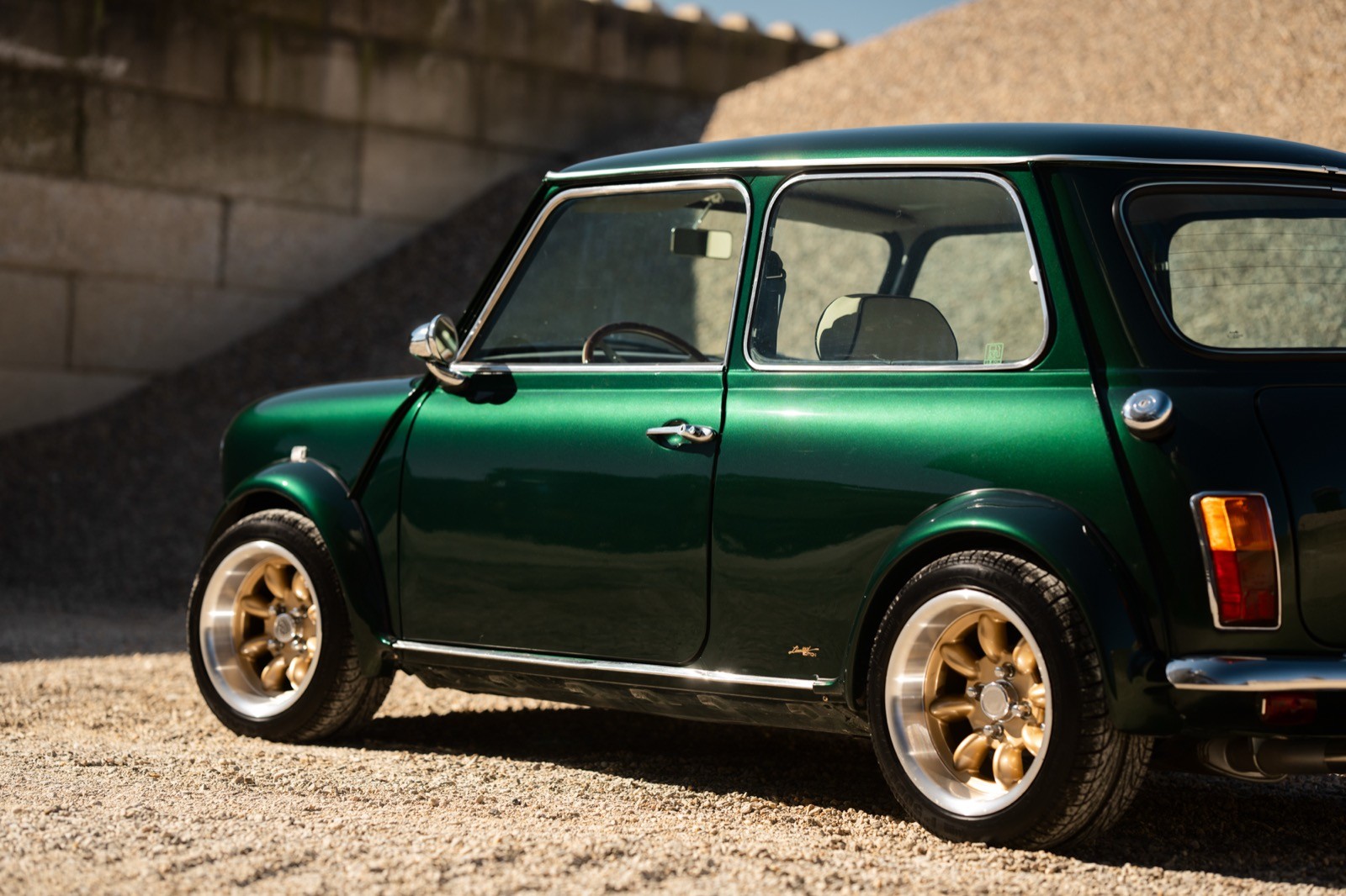 A small, green and black vehicle parked on a sandy surface, with a warm sunset lighting the scene.