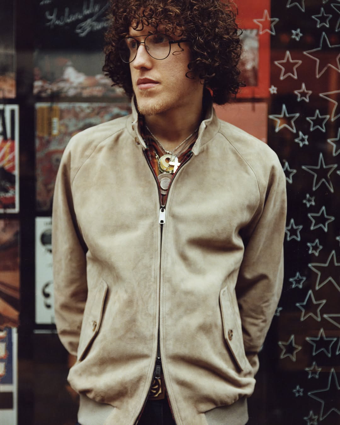 Le mannequin aux cheveux mongs porte un blouson en veau velours beige à double fermeture à glissière et des colliers esprit rock
