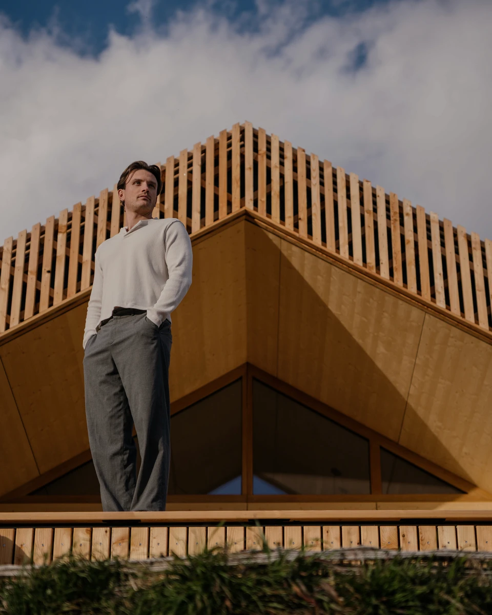 Mann steht auf der Terrasse vor der spitzen Holzlattenfassade des Hoam House unter Wolkenhimmel